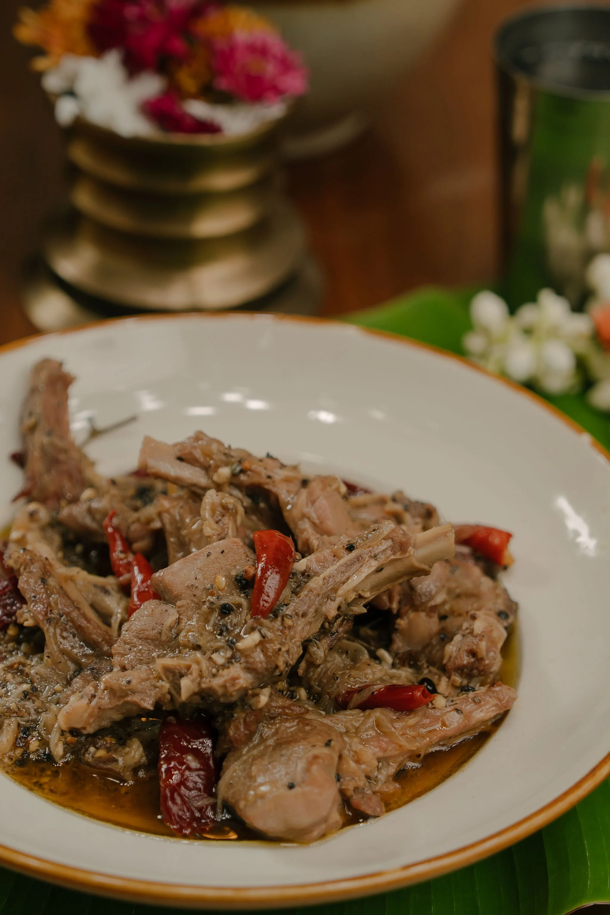 A white bowl containing cooked meat with red chili peppers, herbs, and sauce.