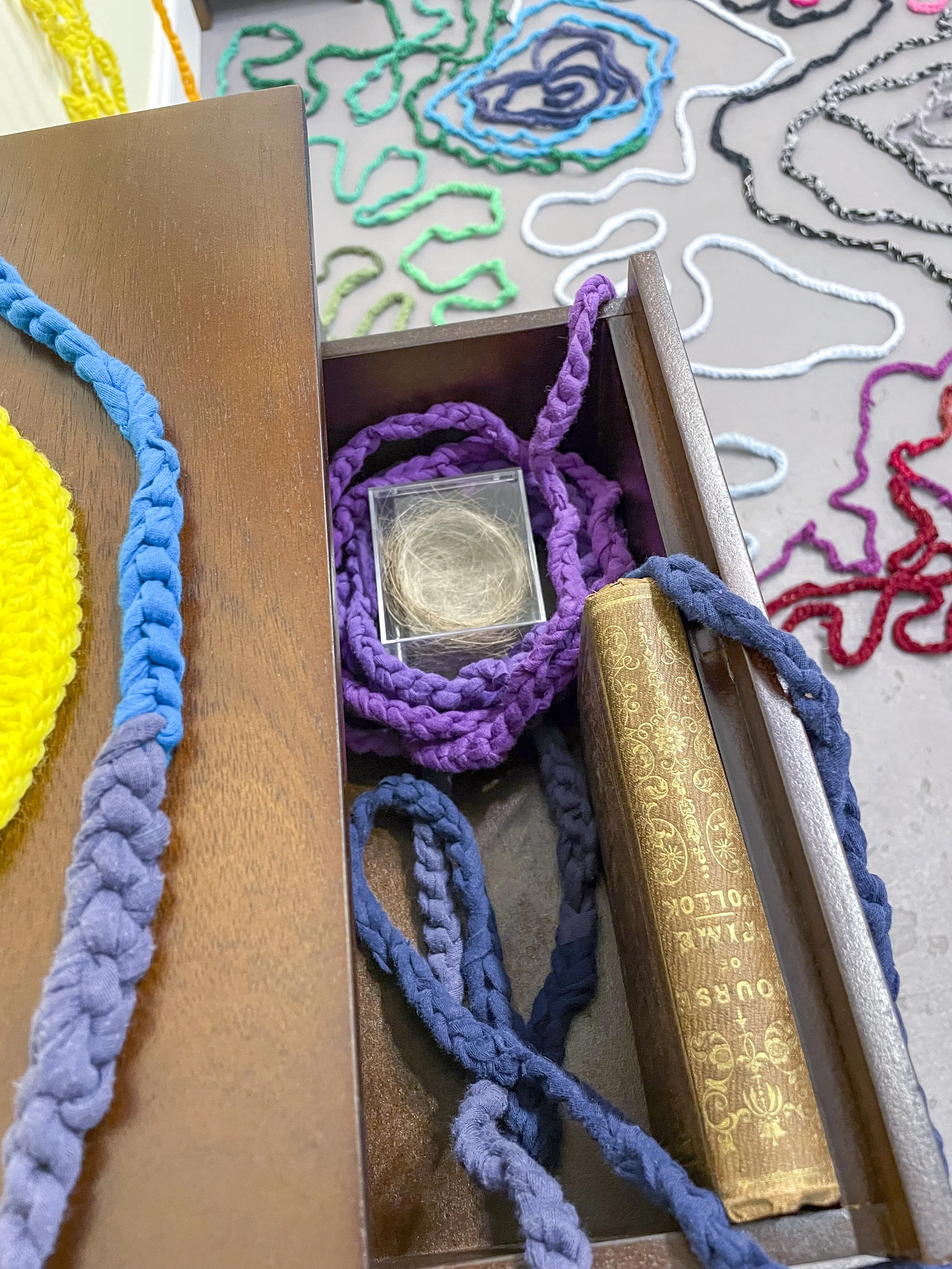  Samantha Mack, detail of  Time and Distance,  2026. Dimensions variable, Two nightstands; two yellow trivets (one made by artist, one made by her great grandmother); threadbare hand-me-downs, cut and crocheted; chiming Regulator clock; antique book 