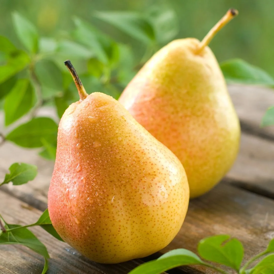 Two ripe pears with water droplets on their skin, placed on a wooden surface with green leaves in the background.