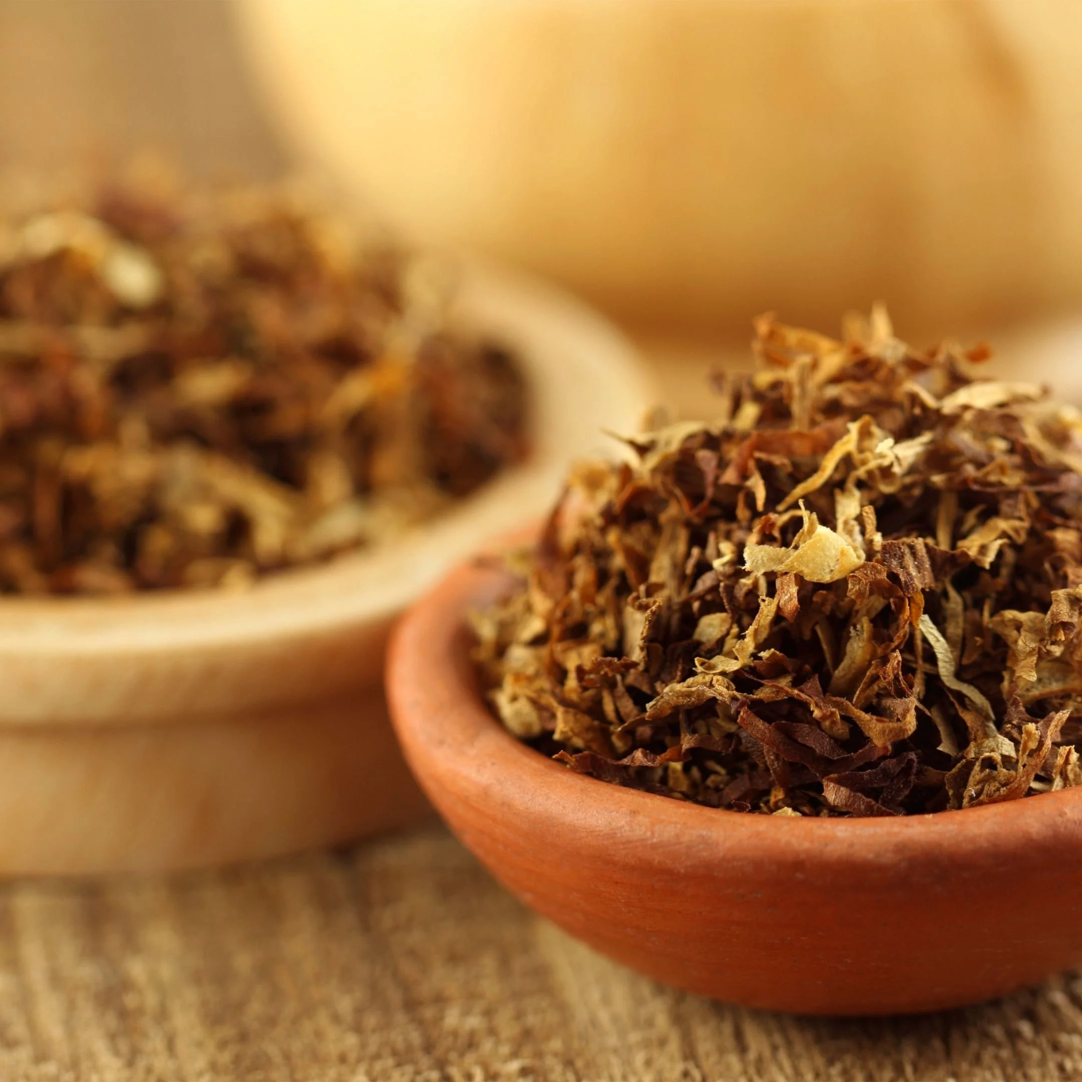 Close-up of dried shredded herbs in a terracotta bowl, with a blurred background of a woven mat.