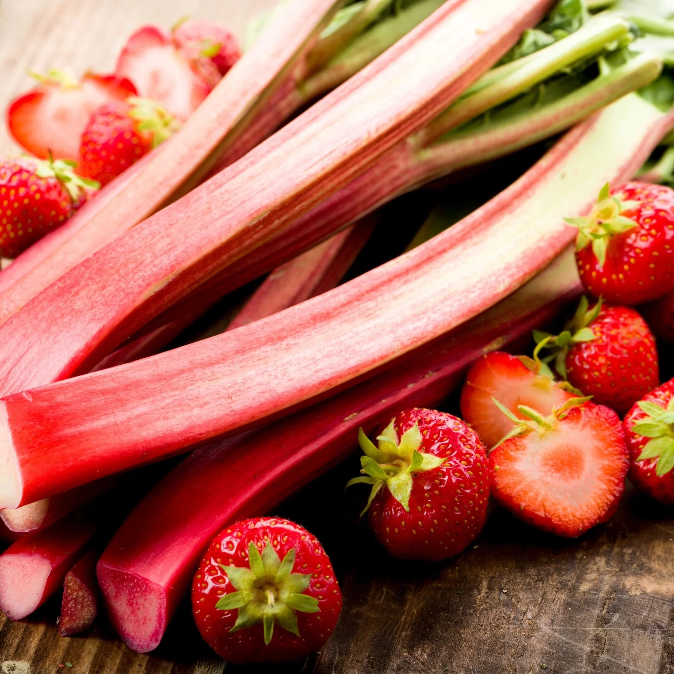 Close-up of fresh strawberries and sliced rhubarb stalks on a wooden surface.