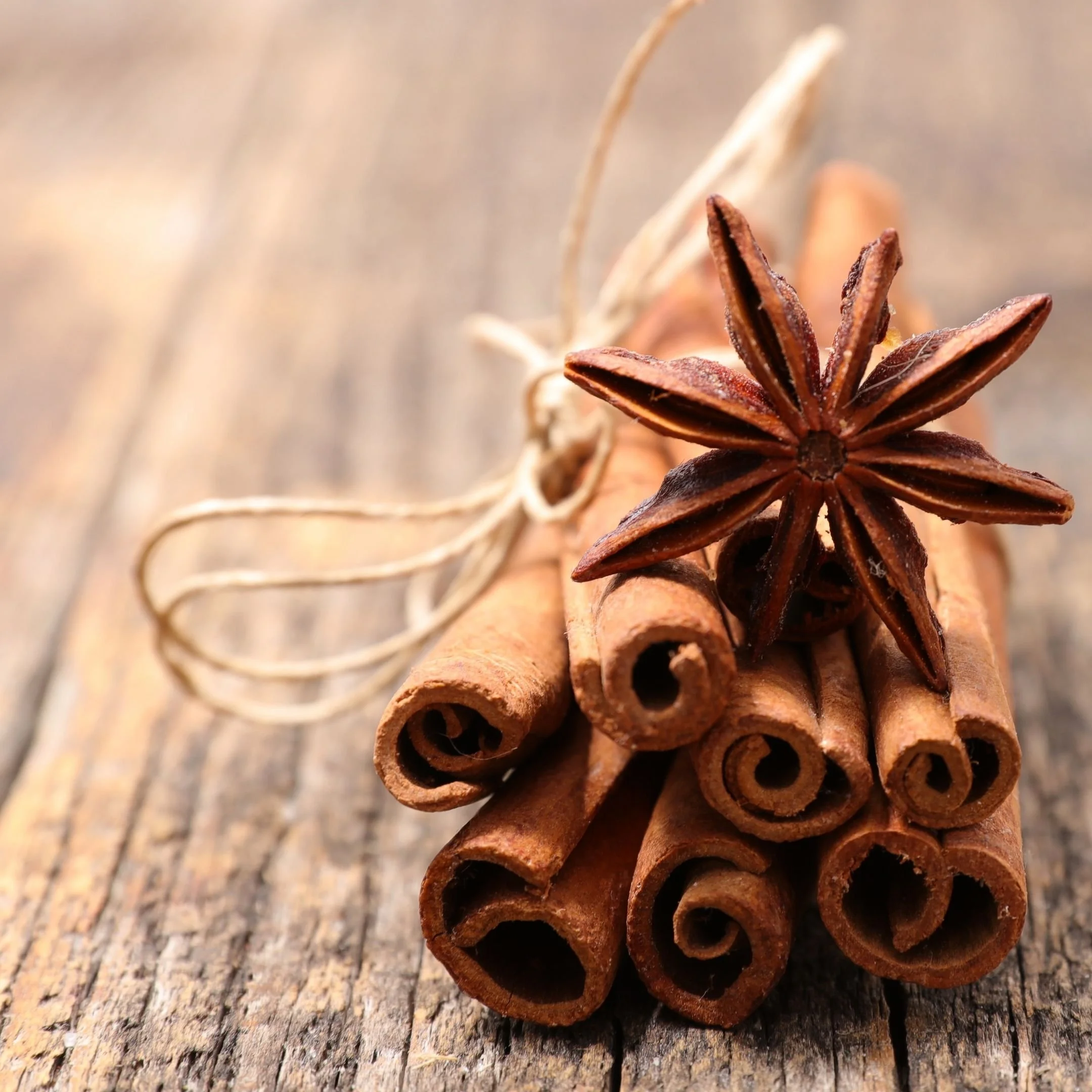 Close-up of a bundle of cinnamon sticks and a star anise on a rustic wooden surface.