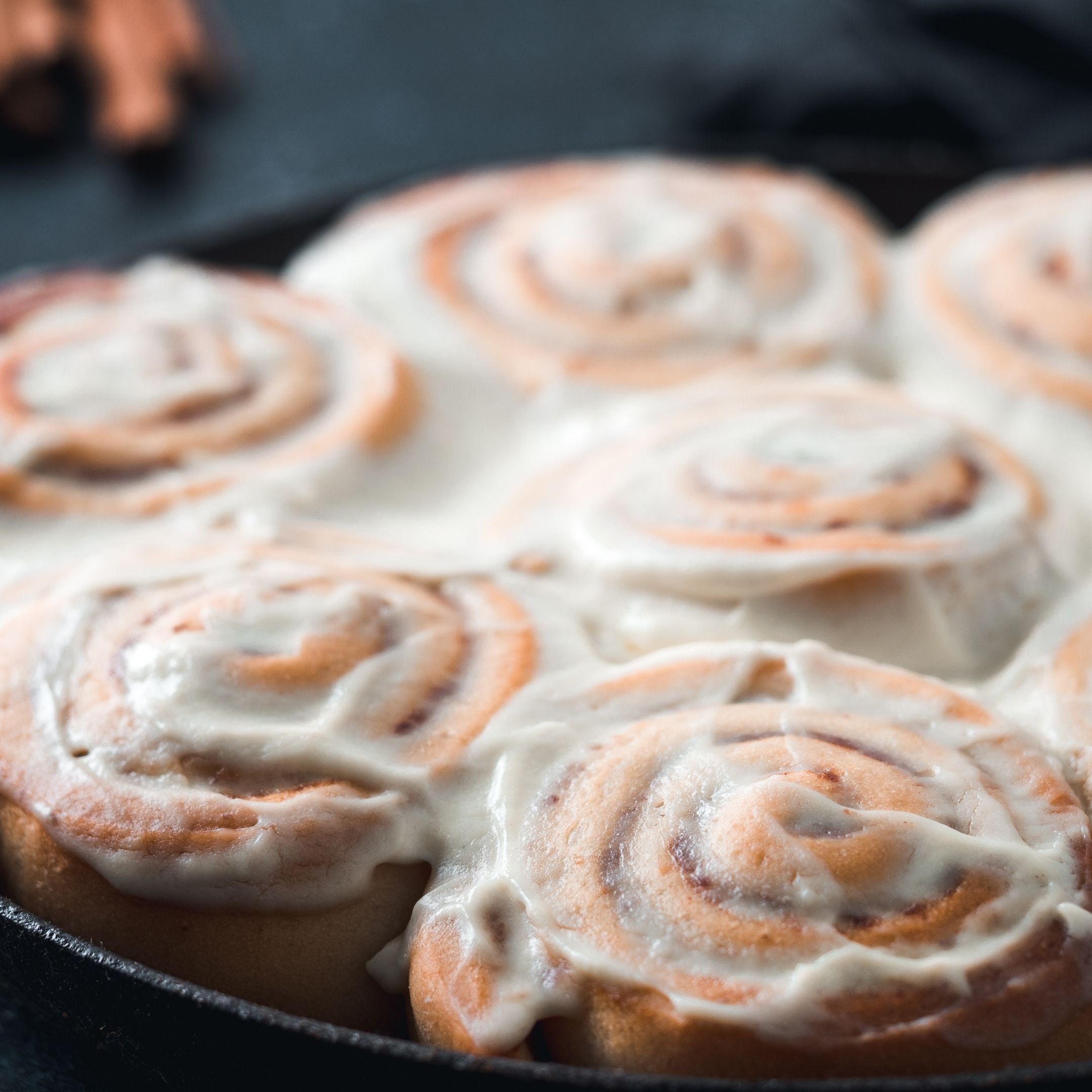 Close-up of uncooked cinnamon rolls with icing in a black pan.