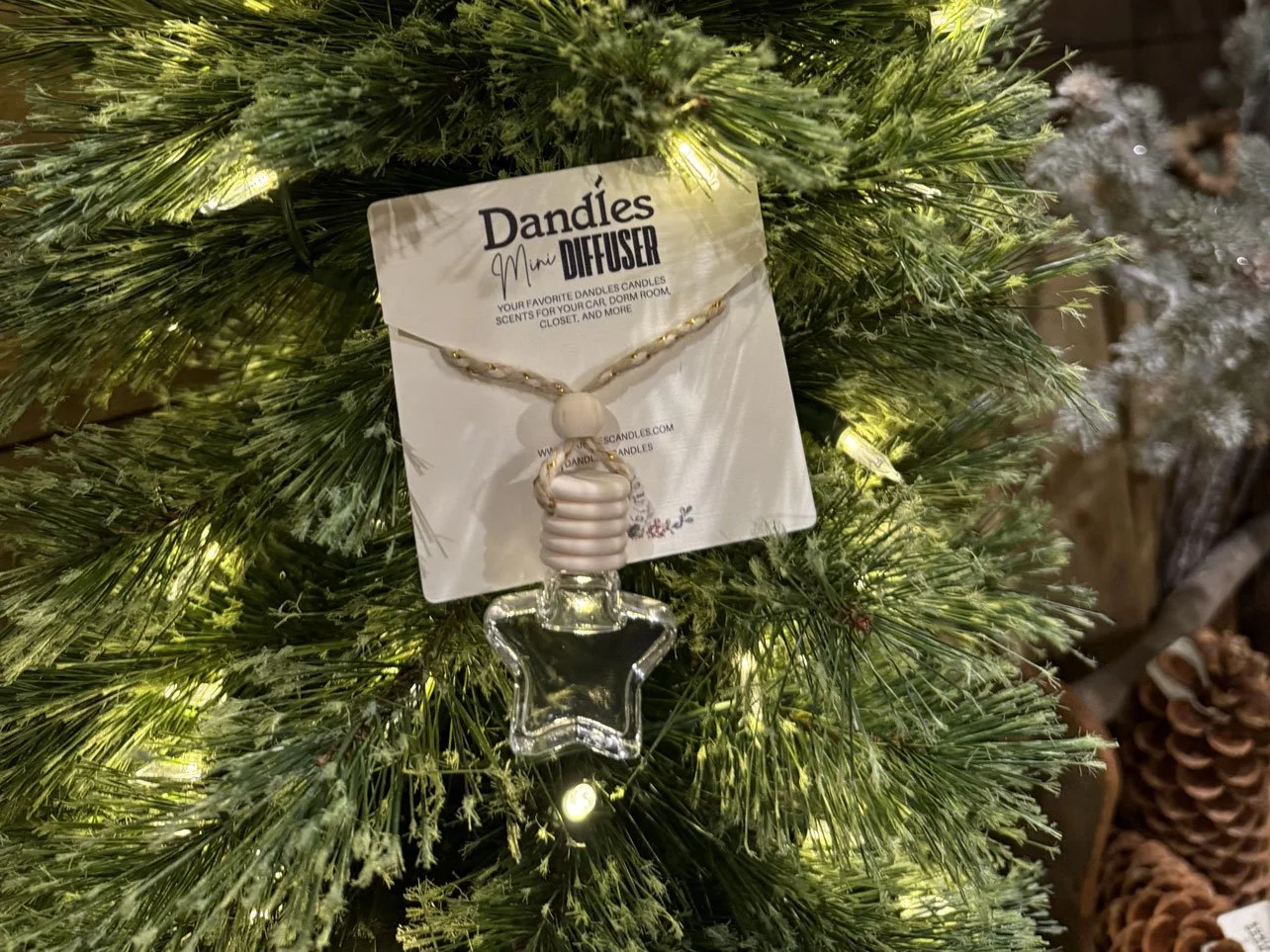A Christmas tree with a hanging star-shaped glass ornament from Dändle's Mini Diffuser, attached to the tree with a string, surrounded by green pine branches and small white Christmas lights.