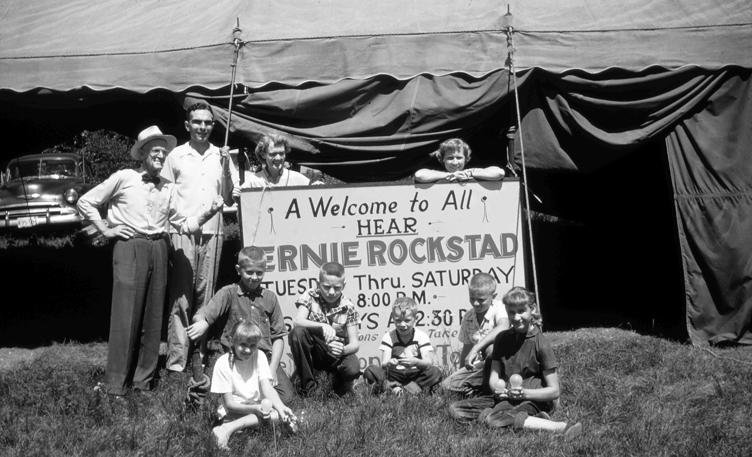 Family and friends gather around the old tent meeting sign.