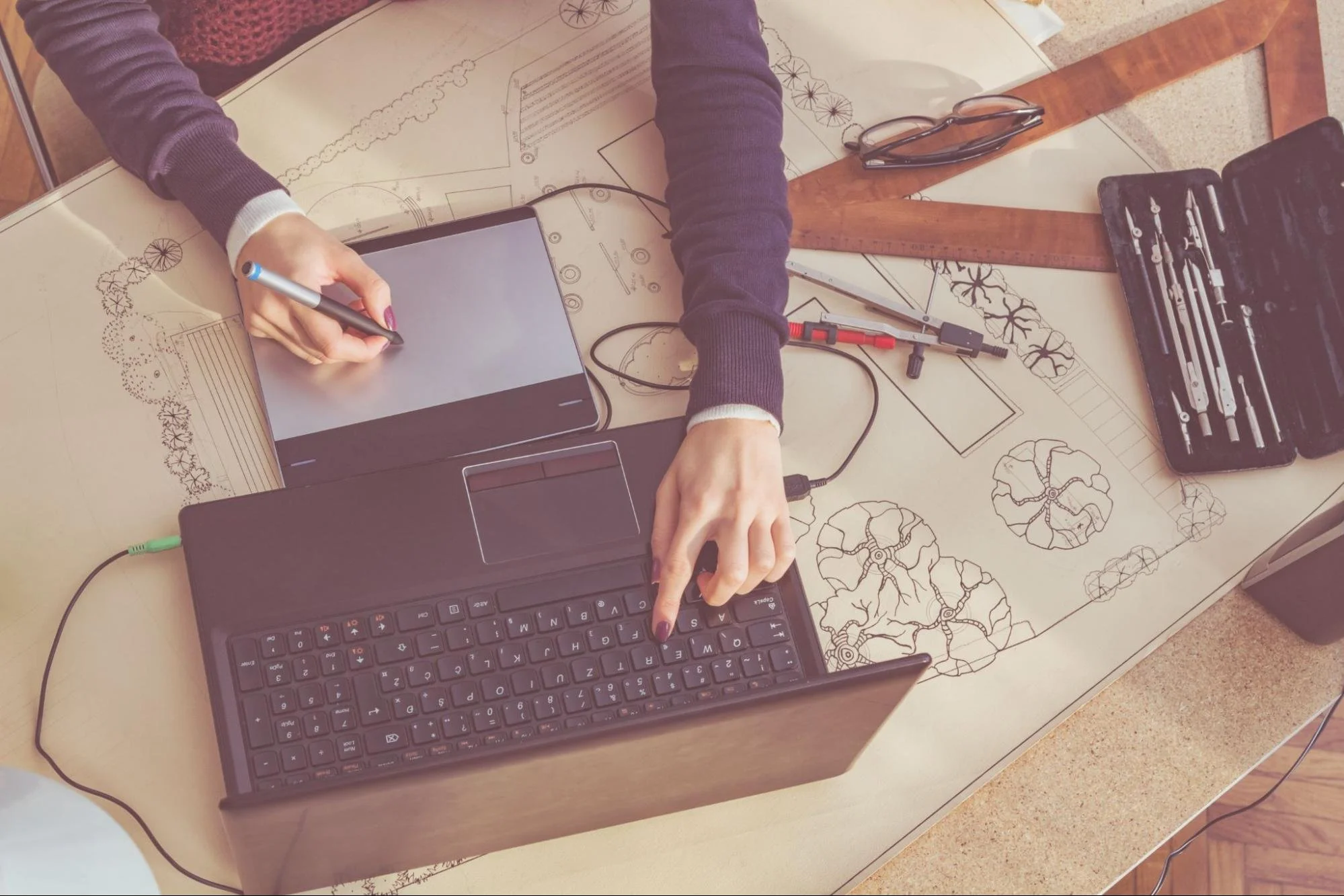 Overhead view of a designer creating a computer-aided landscape architecture plan with digital site modeling and detailed land development drawings