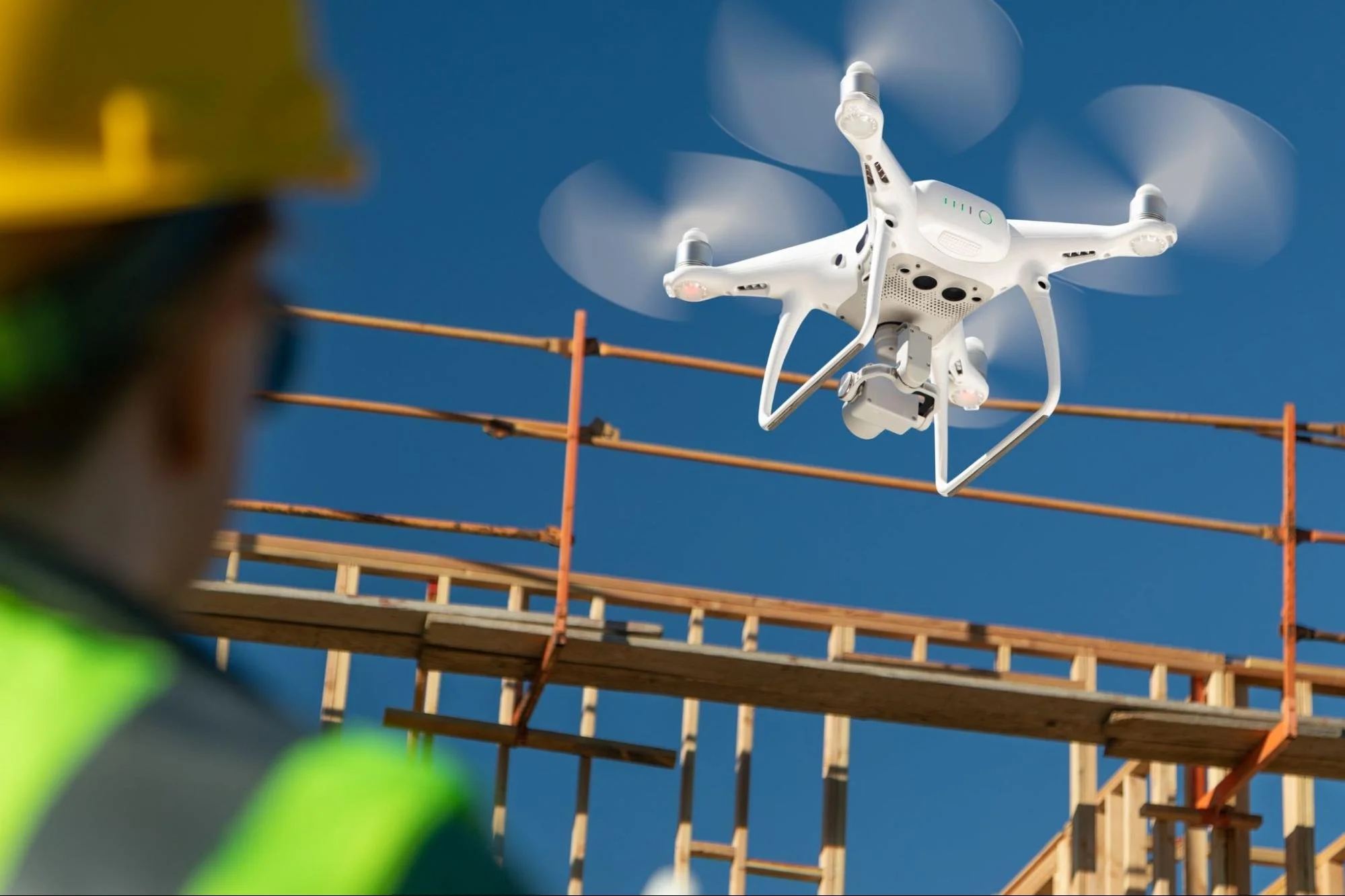 A drone capturing aerial data for an as-built survey at a completed construction site while an engineer monitors operations 