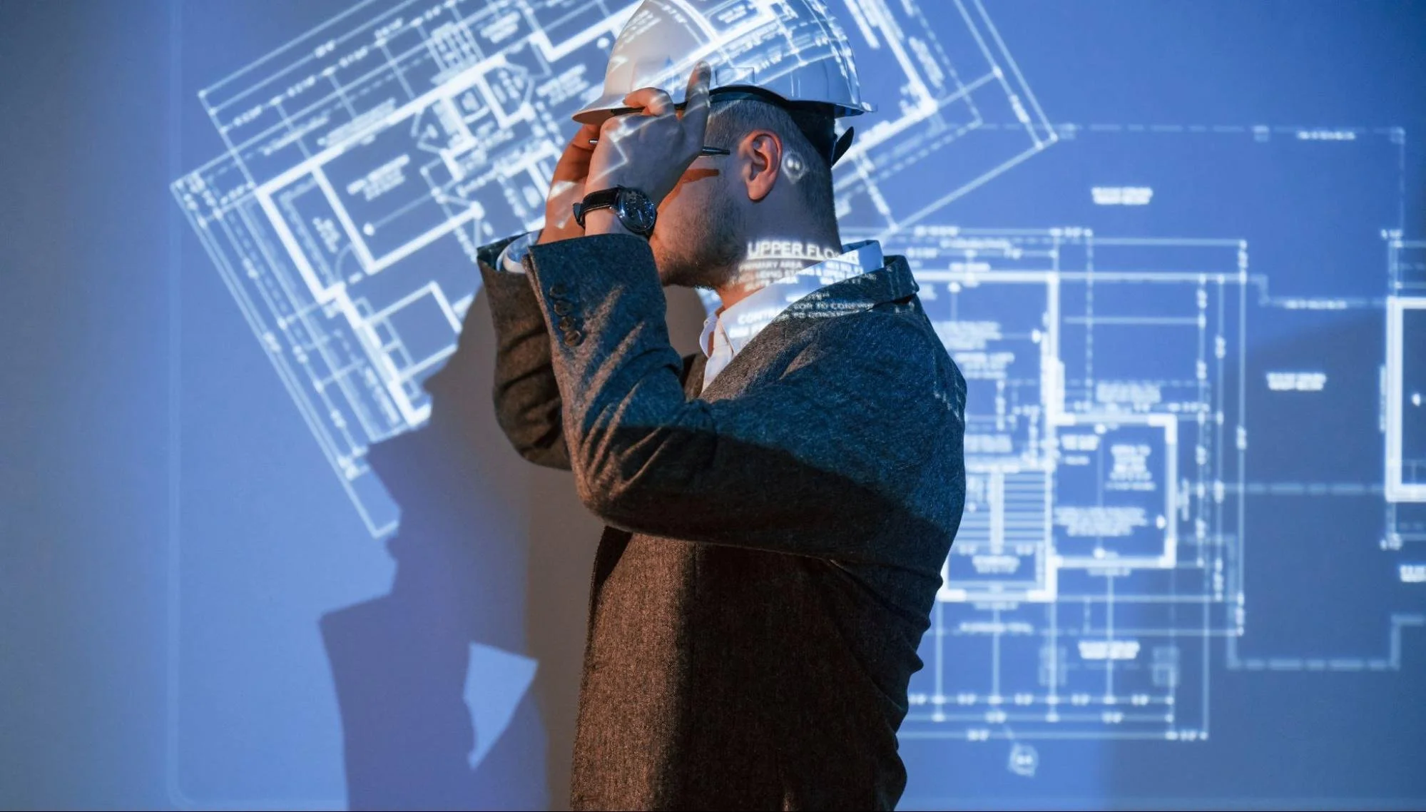 Male architect in a hard hat presenting an interactive floor plan projection for a commercial building survey