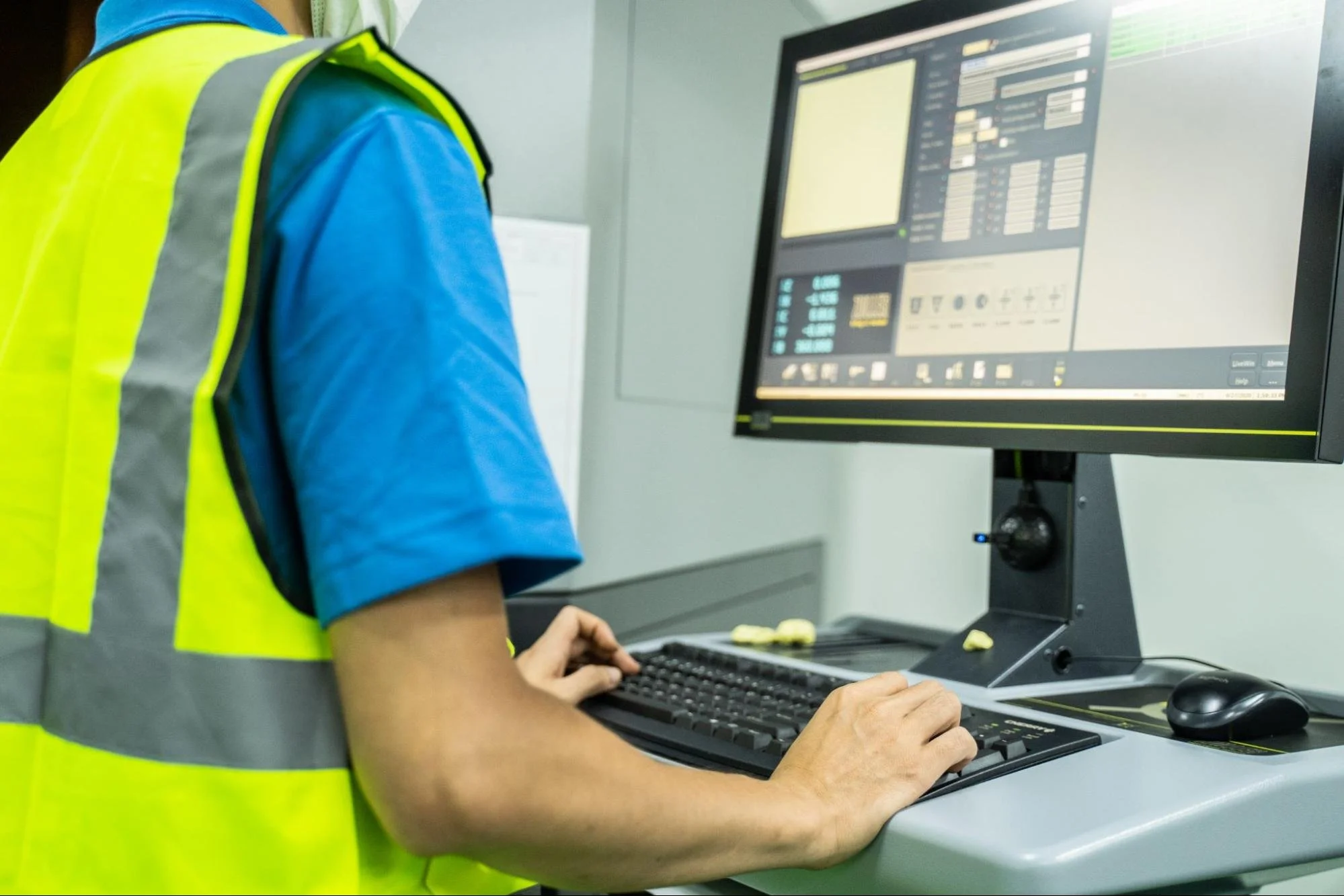 Asian factory technician wearing a safety mask monitoring building systems through computer-aided facility management software