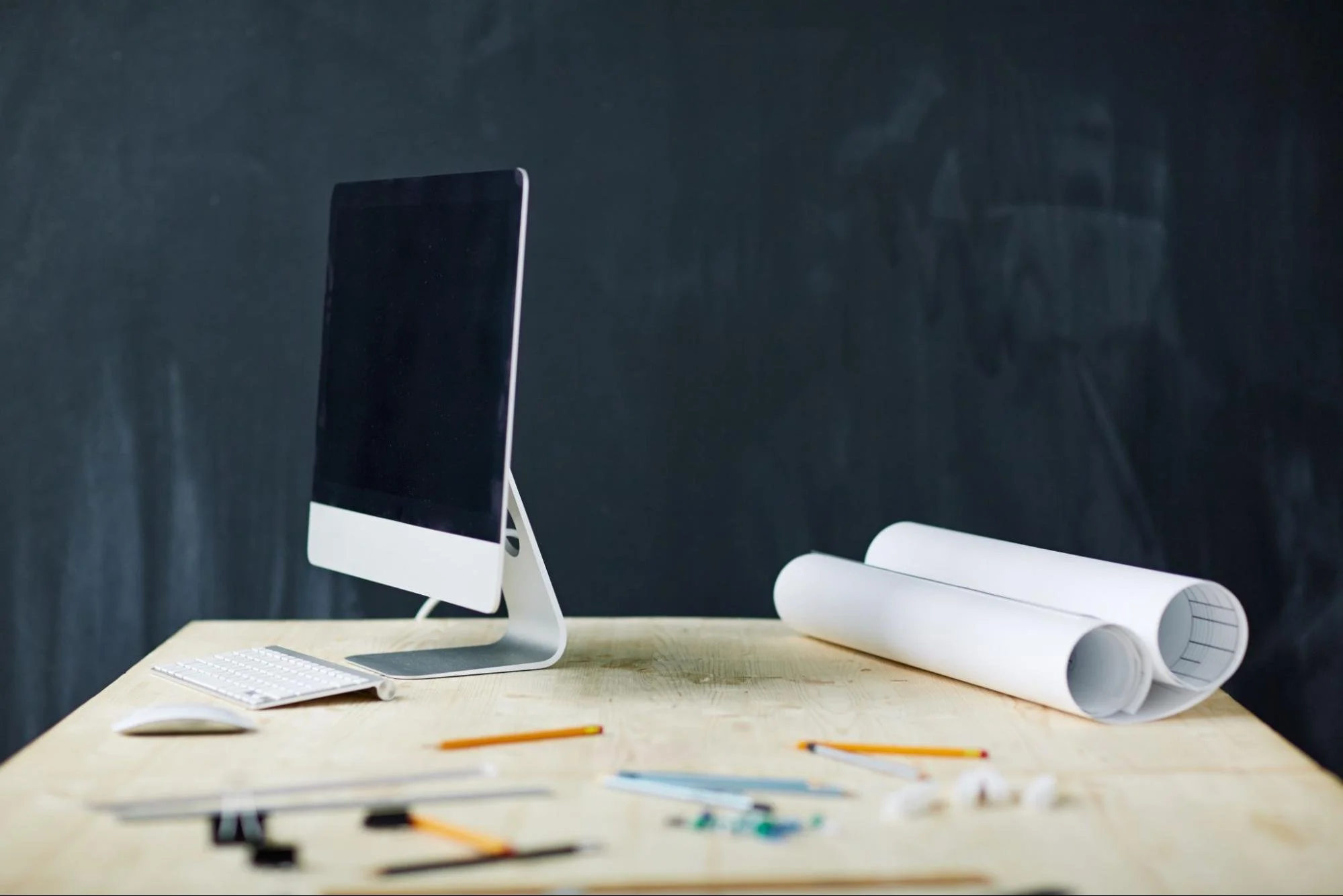 A computer next to blueprints and various architectural tools.