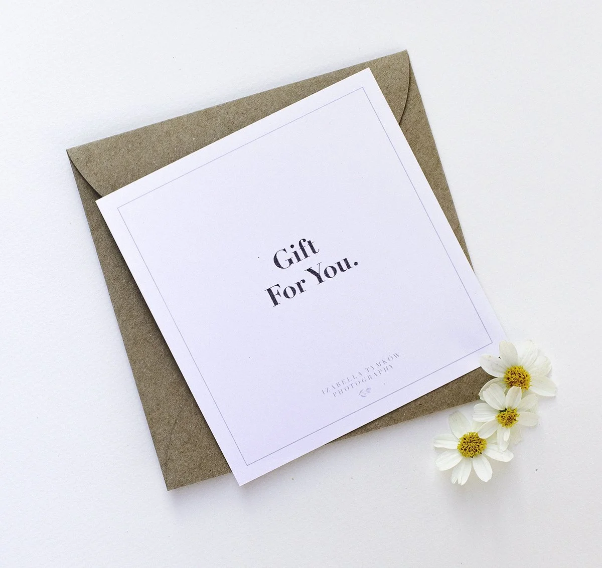 Koperta z kartką z napisem „Gift For You” oraz małymi białymi kwiatami z żółtymi środkami obok niej.