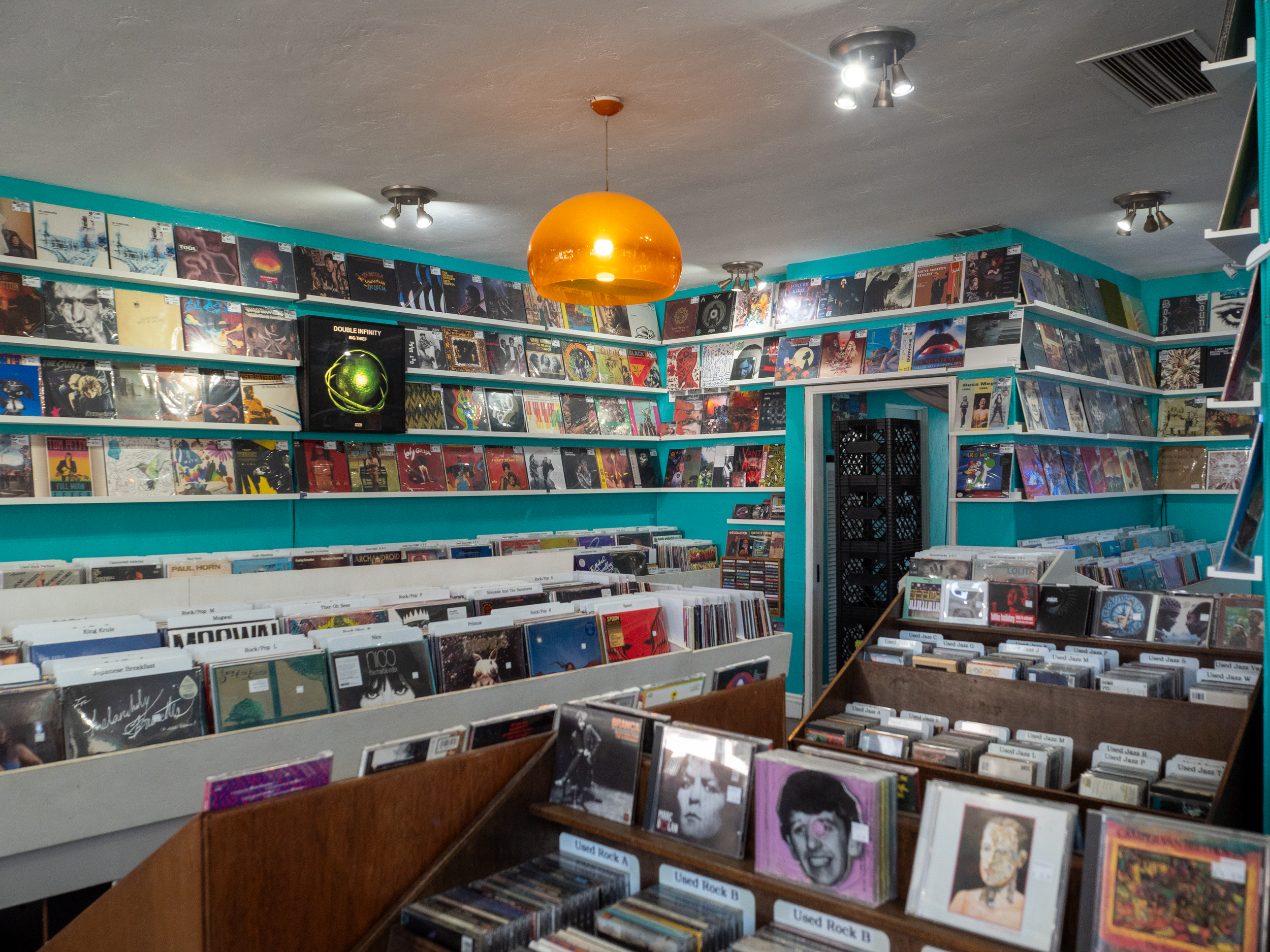 Interior of a record store with shelves filled with vinyl records, a hanging orange pendant light, and ceiling spotlights.
