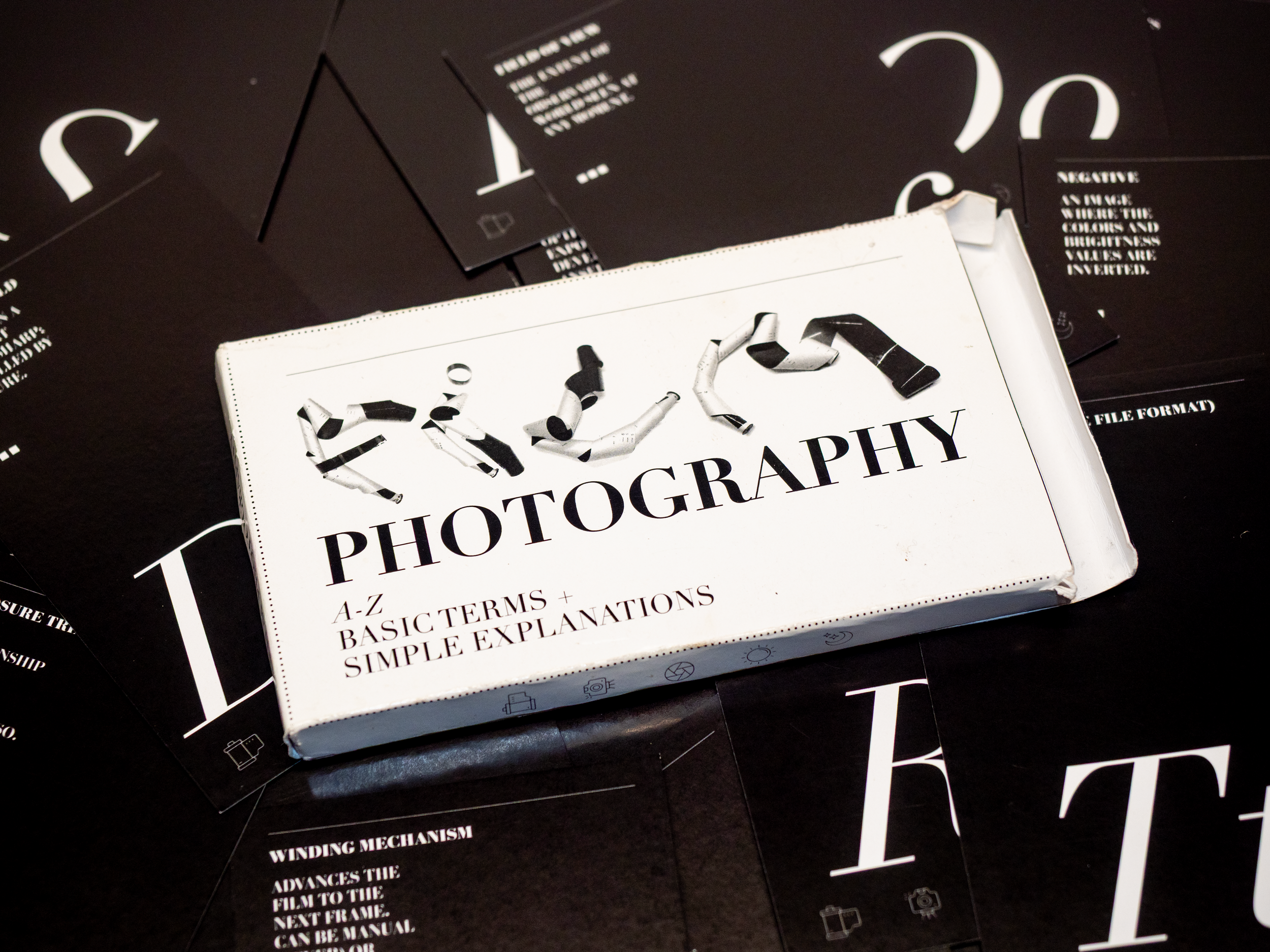 Close-up of a book titled 'Photography' with black and white cover design, placed on a dark surface with scattered papers.