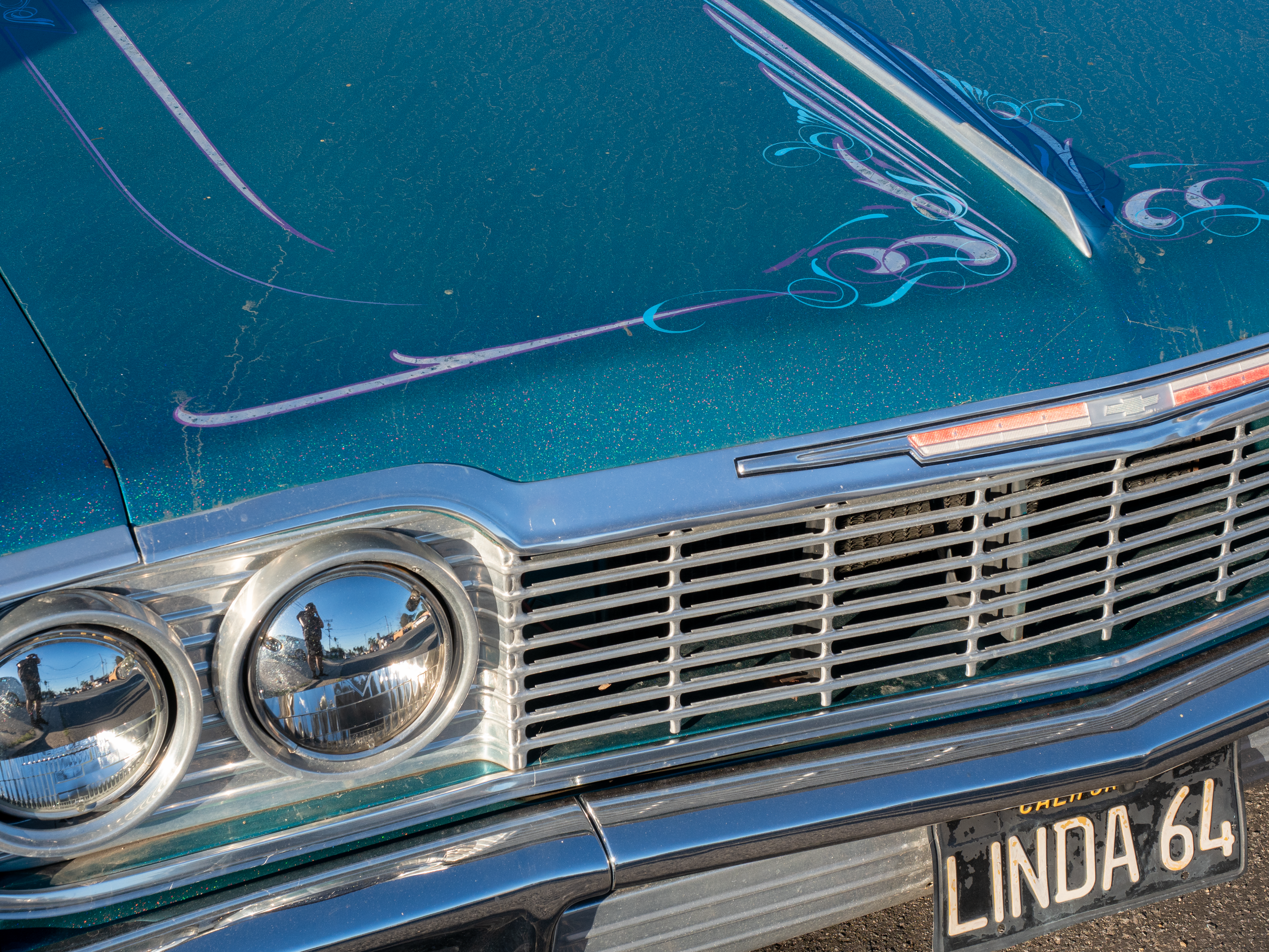 Close-up of the front of a vintage blue Chevrolet car with glittery paint, chrome grille, and four round headlights, parked outdoors.