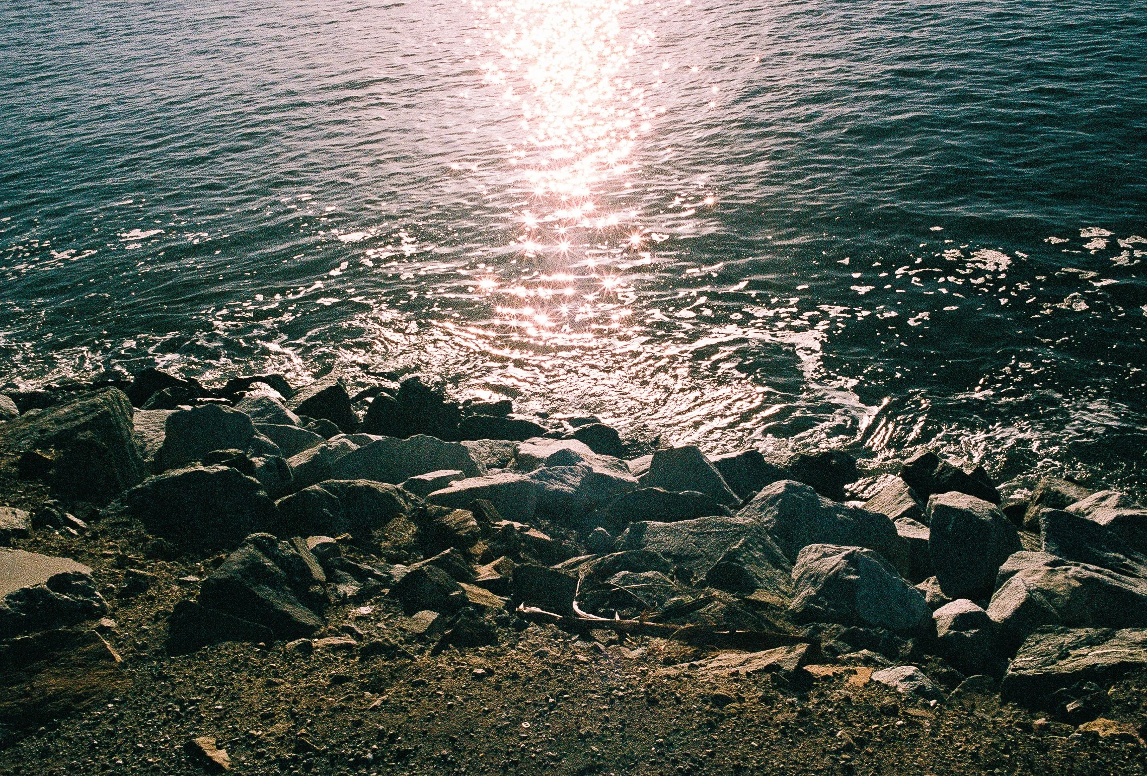 Sunlight reflecting on the water near a rocky shoreline.