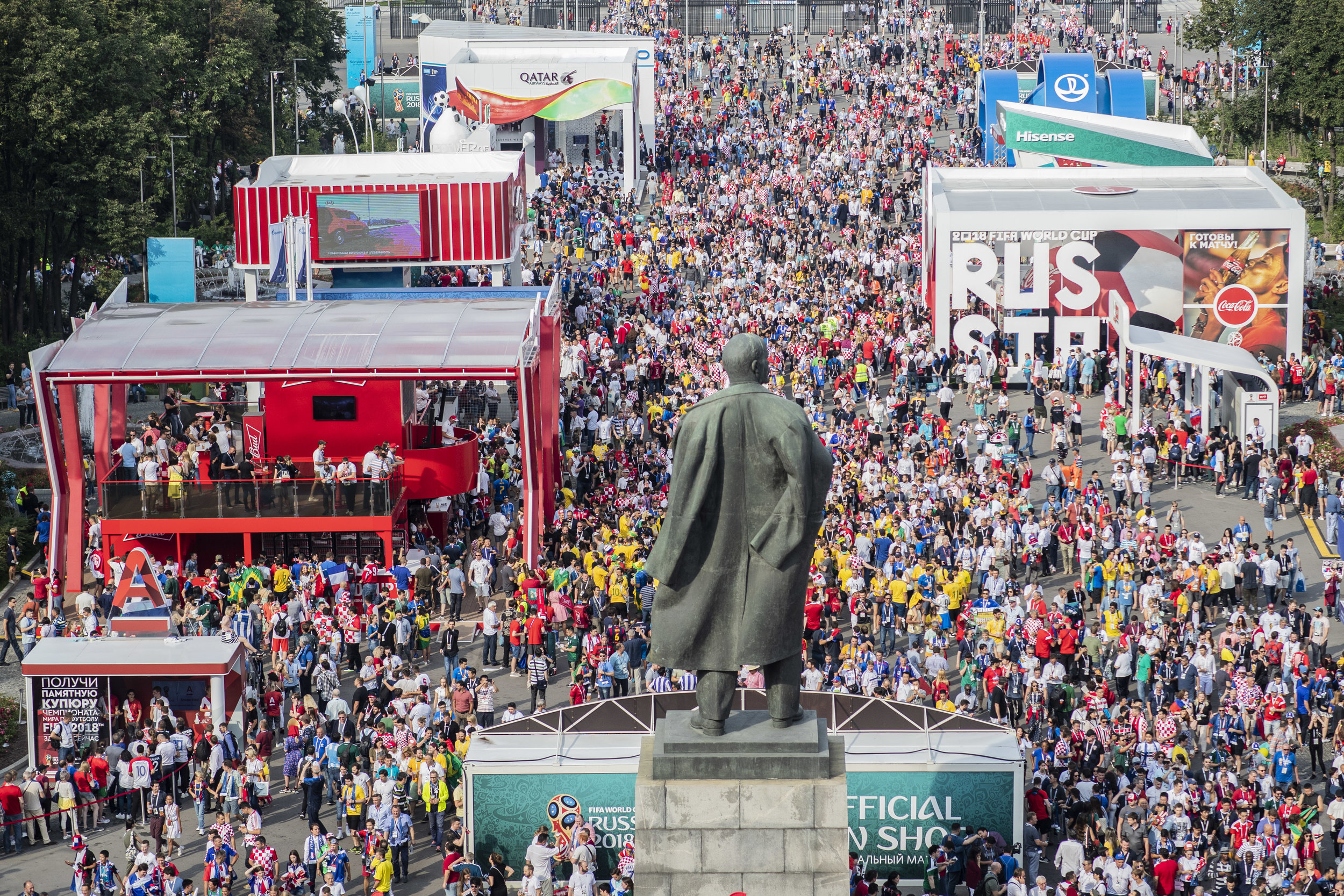 Fans of all nations enter Luzhniki stadium passing by Lenin's statue and an alley filled with sponsors' pavilions in Moscow