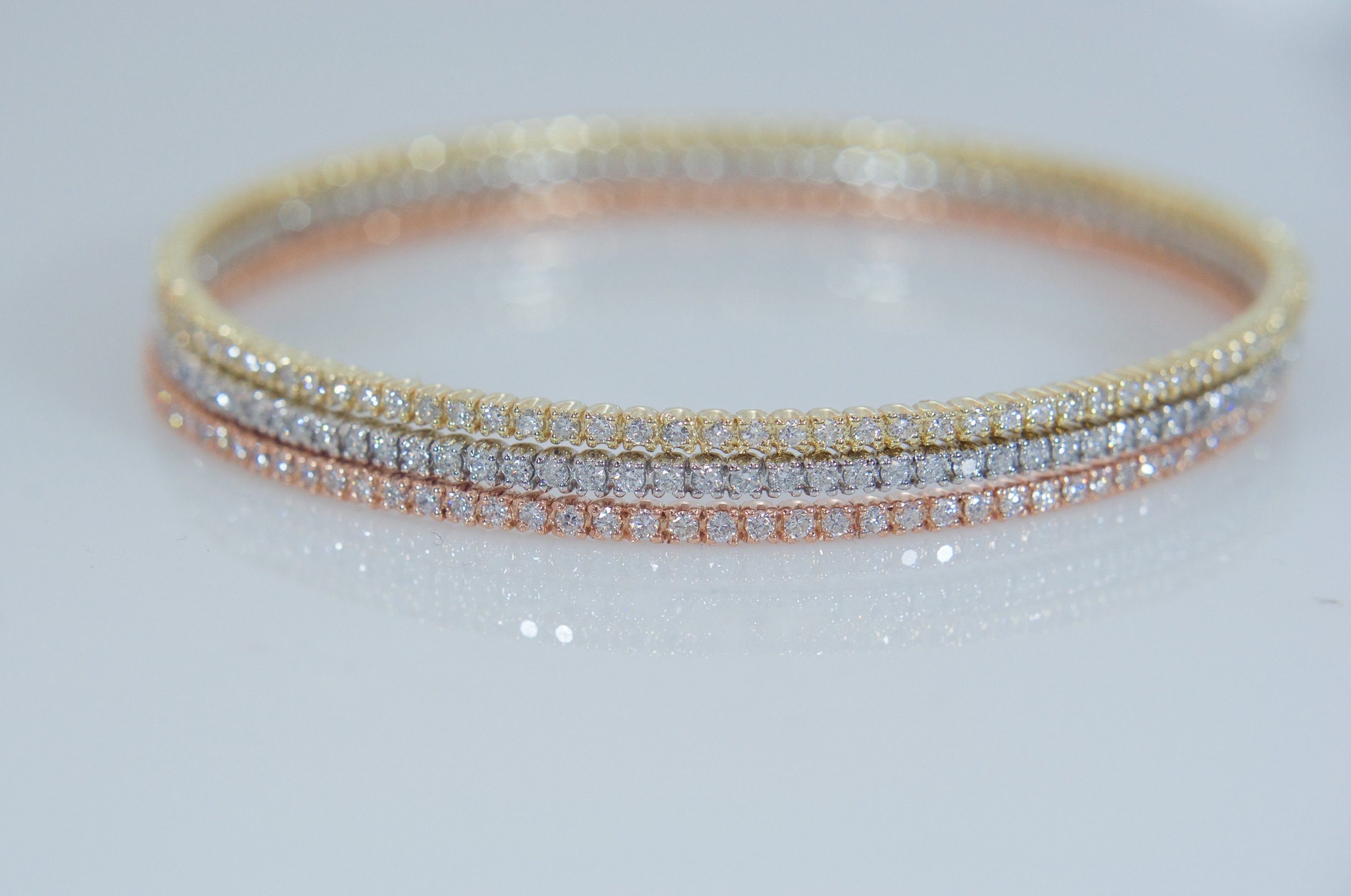 Three diamond eternity bangles in yellow, white, and rose gold