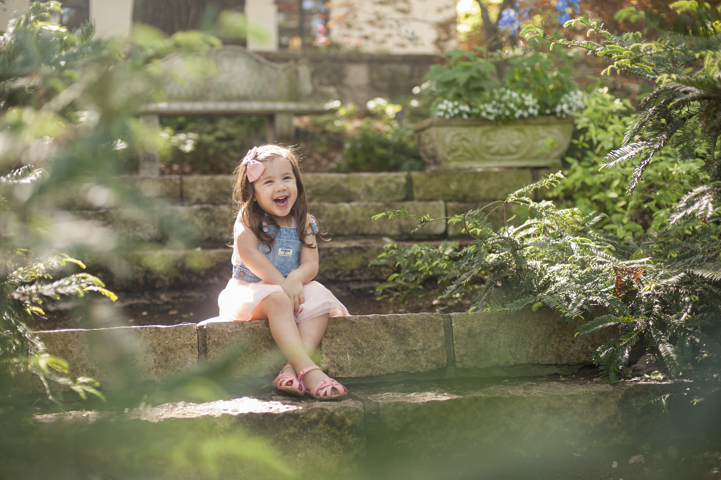 Toddler smiling amidst the greenery. Childrens portraits at the Dallas Arboretum.