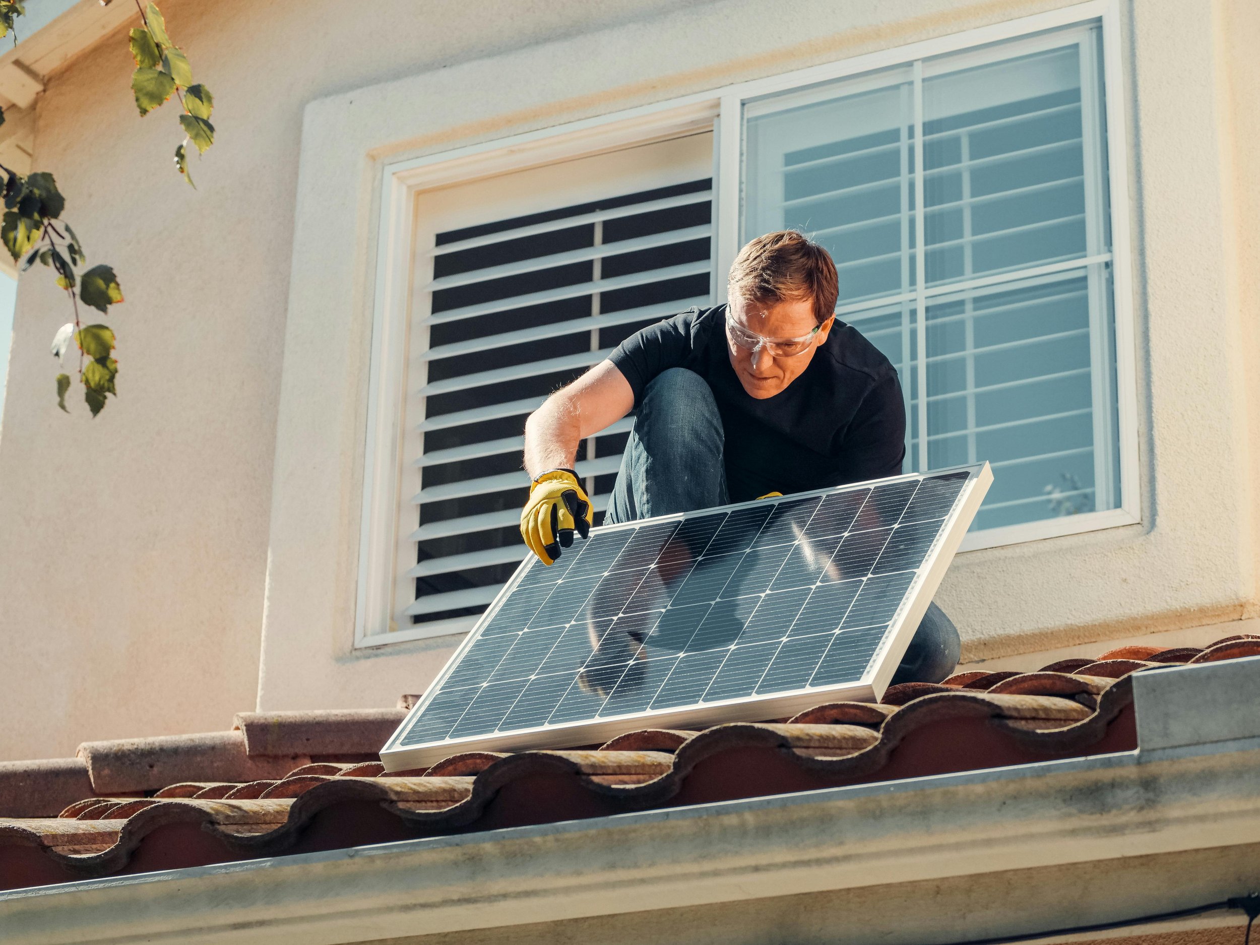 A man installing a solar panel on a house rooftop during daytime.