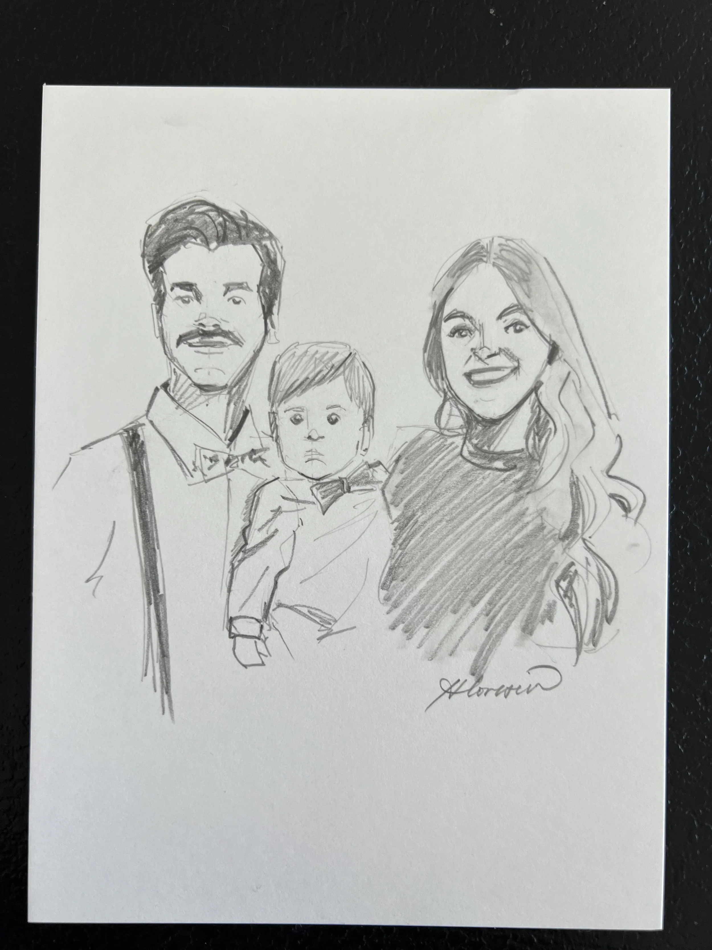 A hand-drawn sketch of a family of three, including a man with a mustache and bow tie, a woman with long wavy hair, and a young boy with short hair, all smiling and dressed nicely.