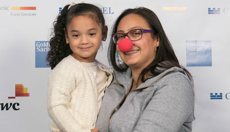 Woman Holding a Child While Wearing a Clown's Nose