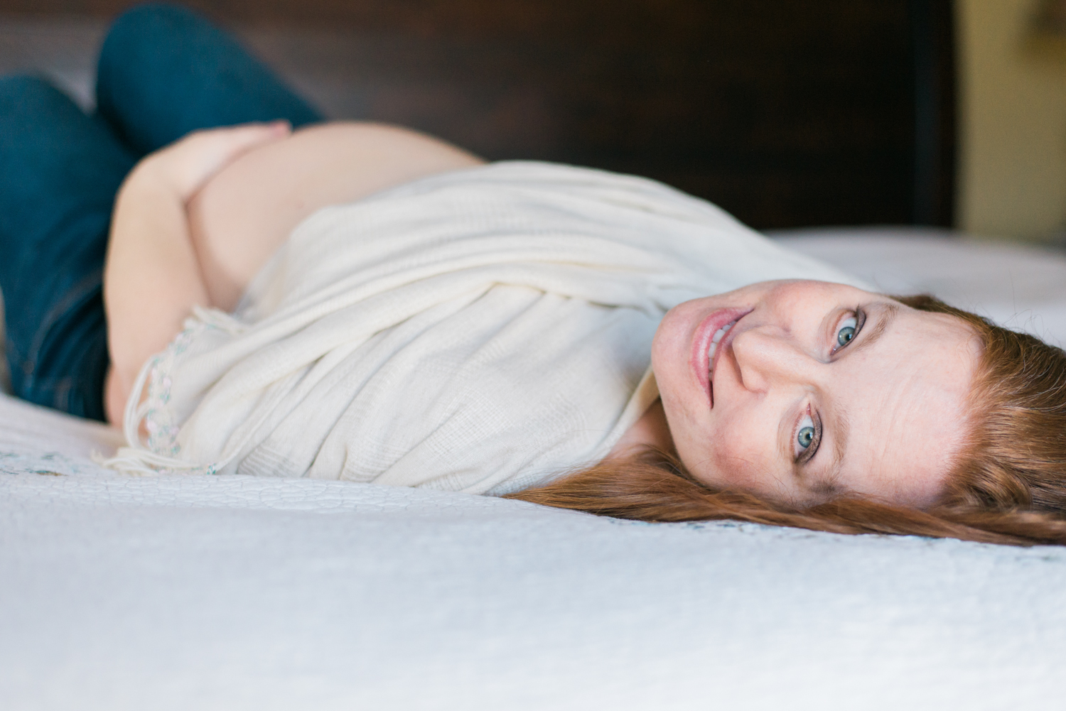 Buckinghamshire Indoor Maternity session shows intimate moment of mom holding her pregnant belly while laying on her bed.