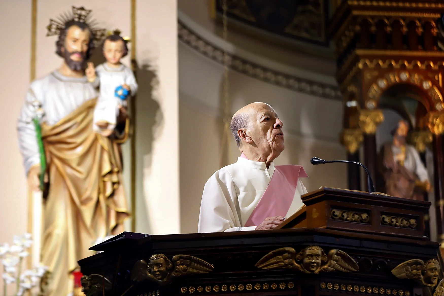 Deacon Javier Pineda addresses parishioners at St. Joseph at the lectern in front of a statue of Joseph and baby Jesus.