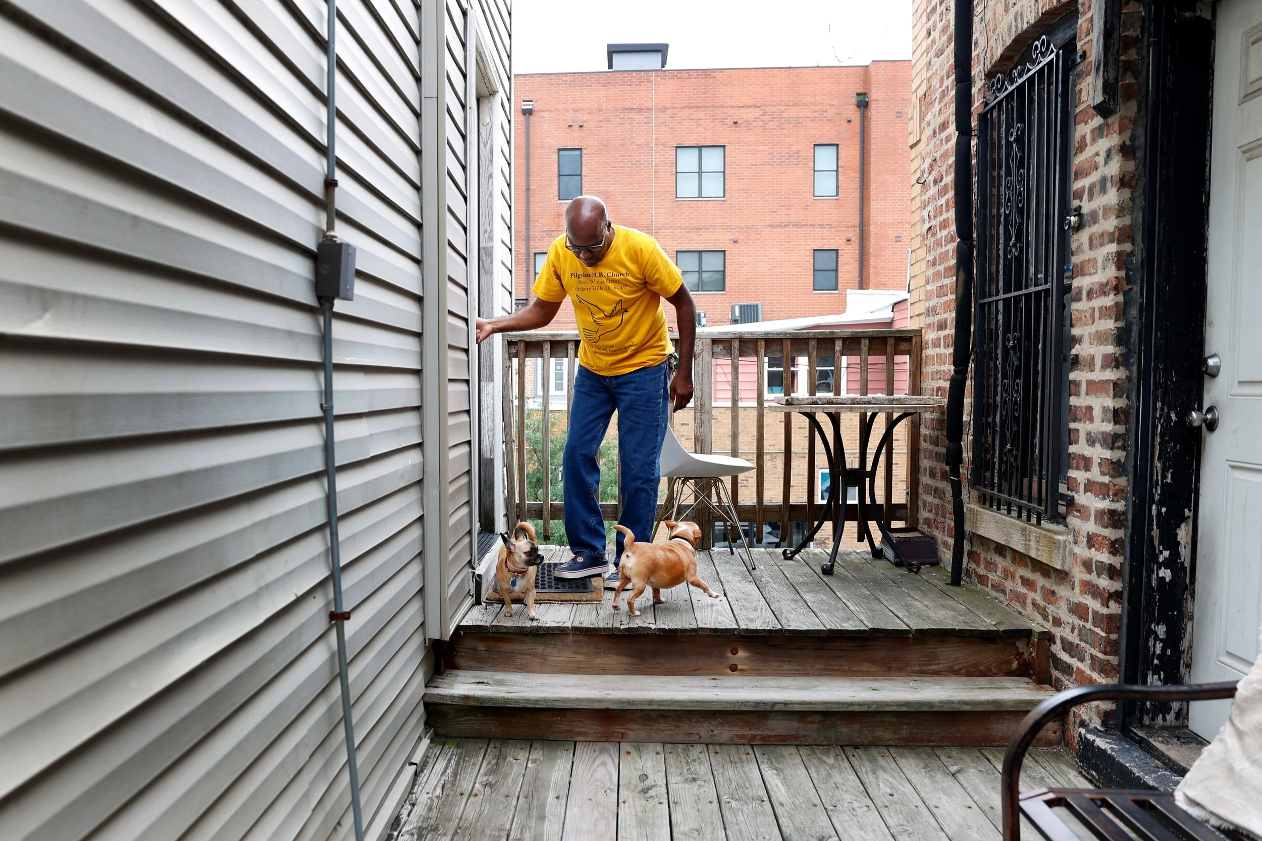A man lets his dogs into his apartment from the outdoor patio.