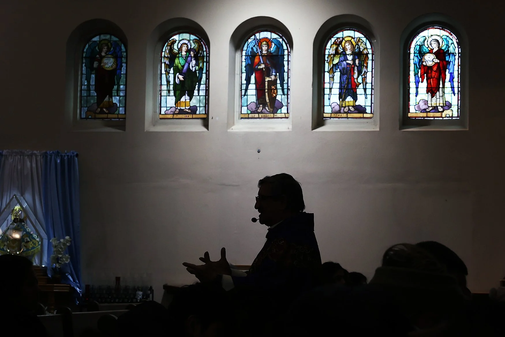 The silhouette of Father Pedro Antonio Lopez is seen below five stained glass windows depicting angels at St. Joseph Parish.