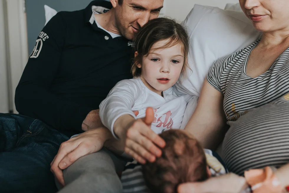 mum+and+dad+and+big+sister+looking+at+newborn+baby+in+hospital+in+melbourne+birth+photographer+Jenny+rusby+photography