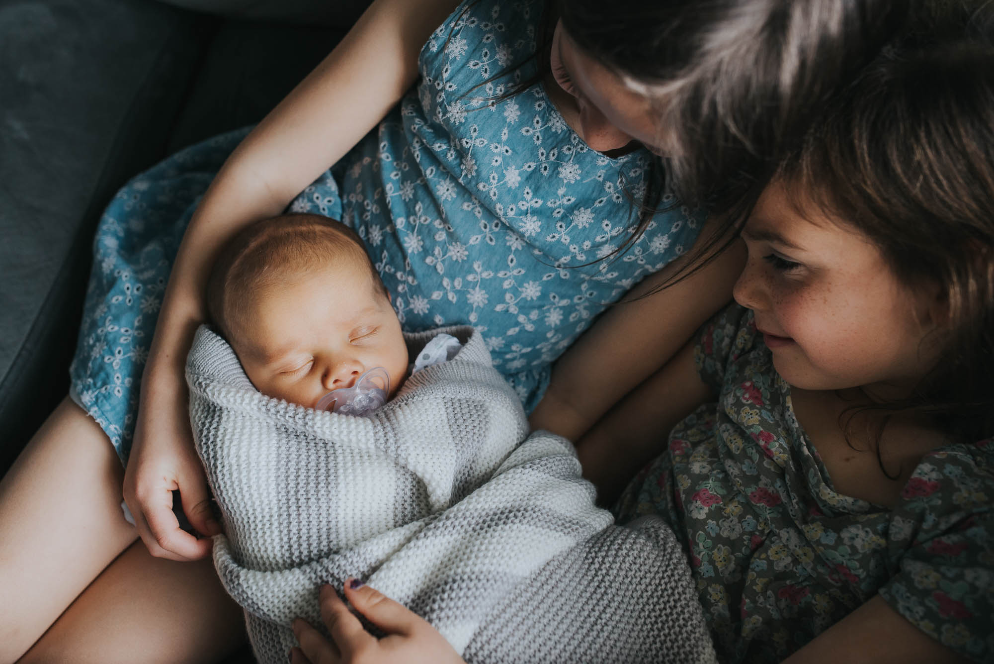 newborn baby being held by big sisters at a newborn photo session