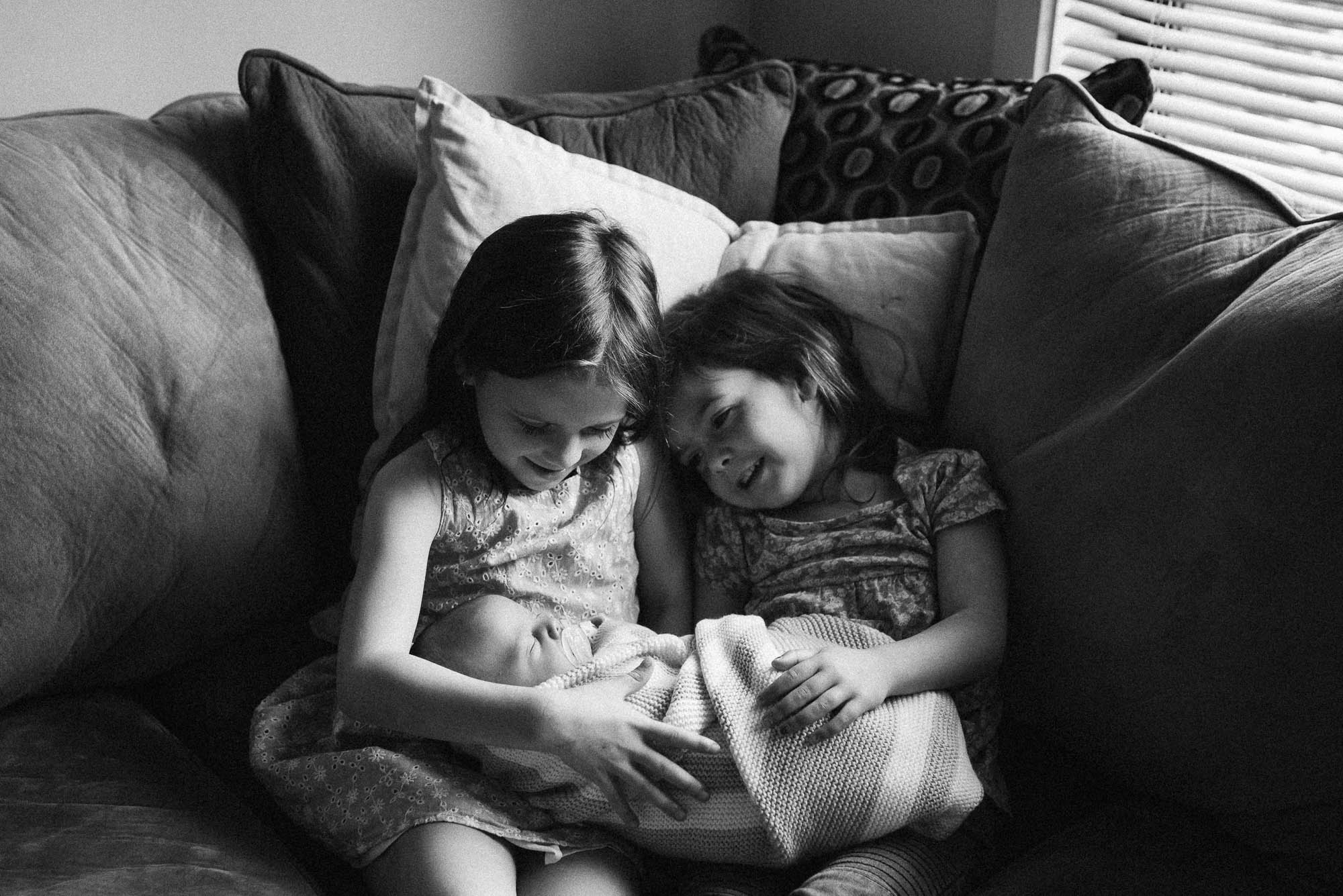 big sisters holding baby brother at a newborn photo session