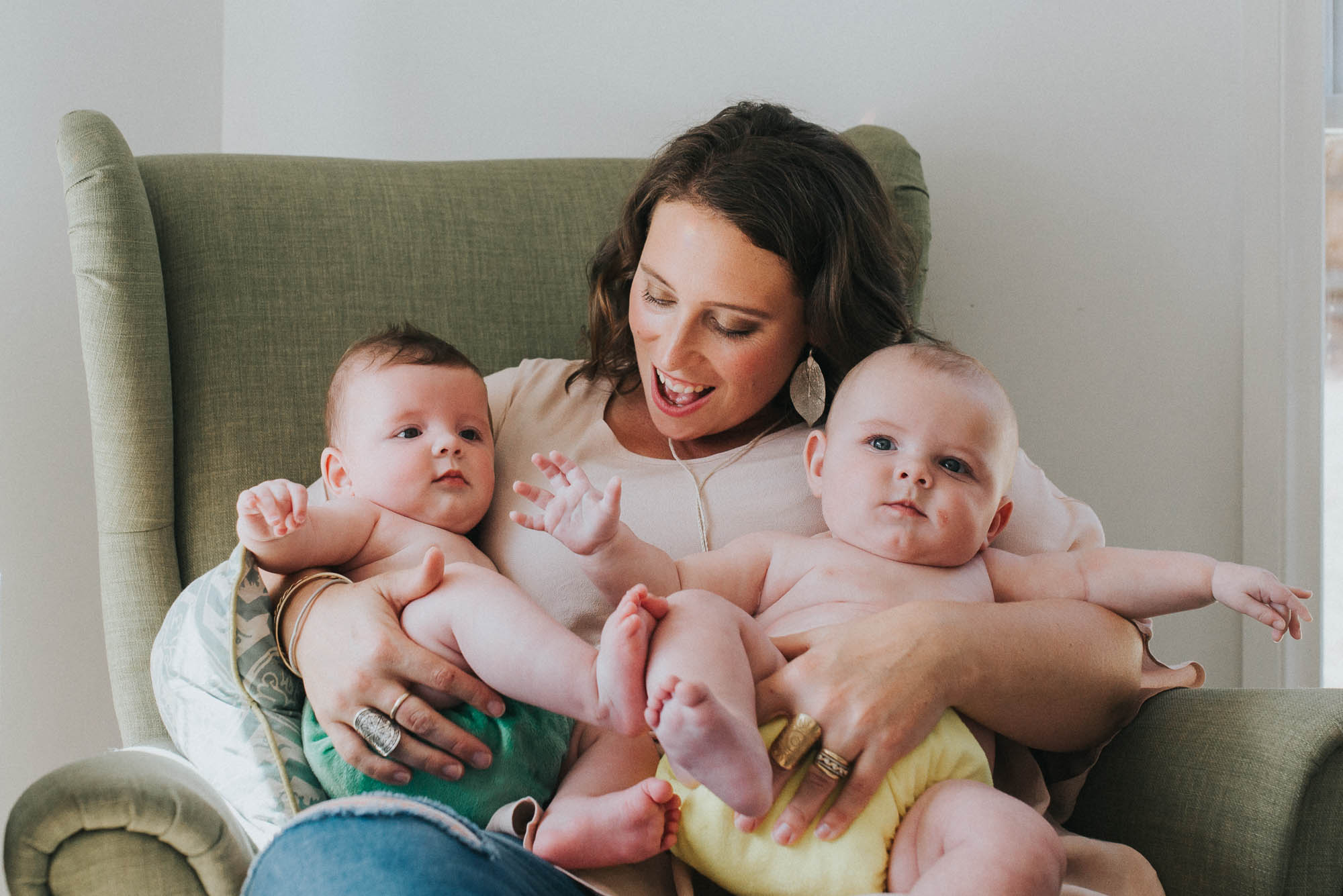 mum smiling while holding twin babies on a chair