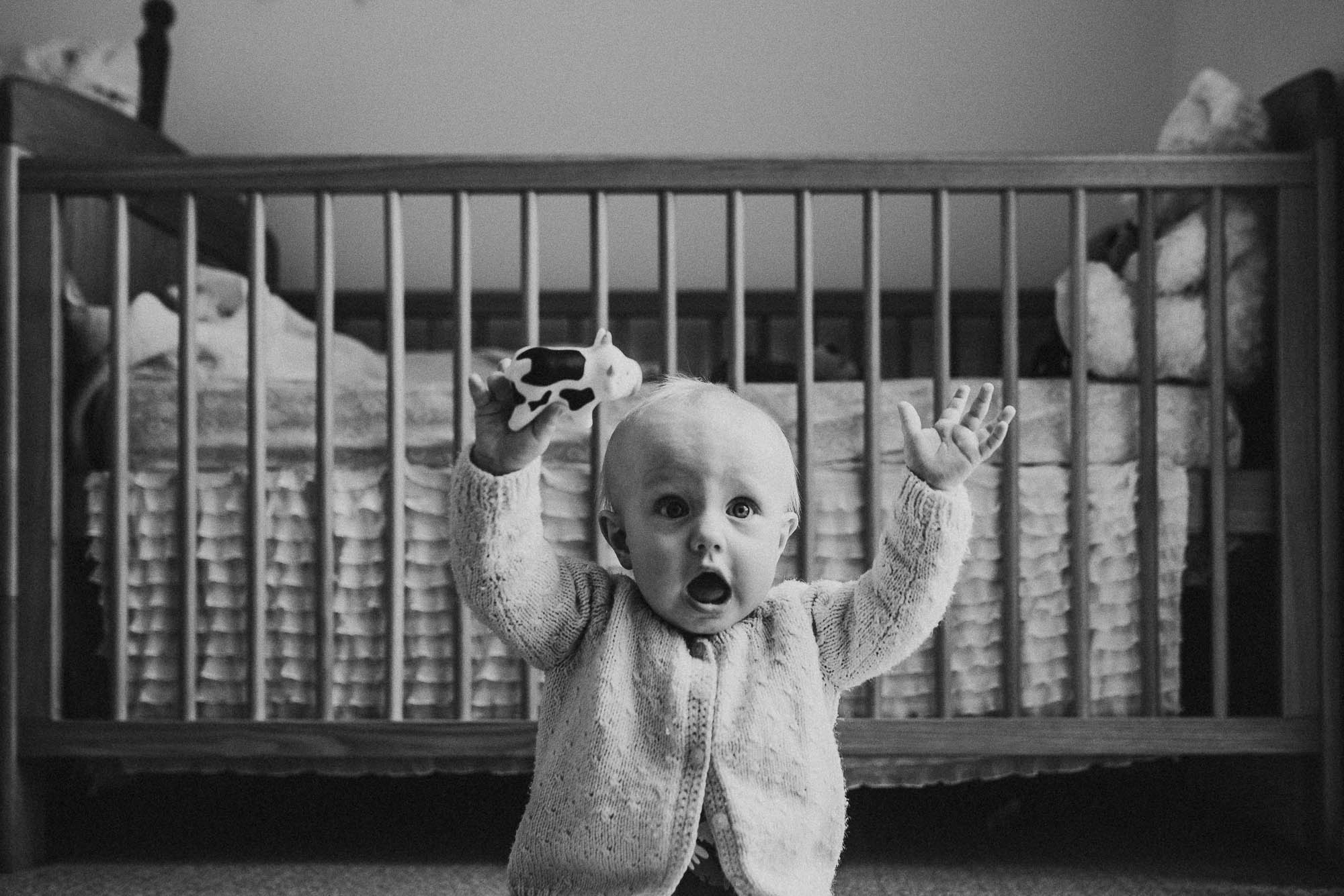 baby-sitting-with-arms-up-in-the-air-in-front-of-cot-in-black-and-white