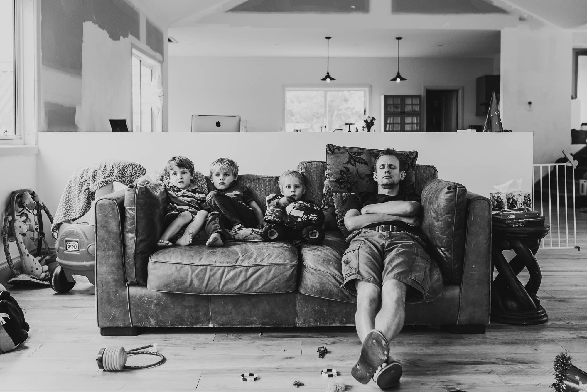 dad-asleep-on-sofa-with-children-awake-next-to-him-and-toys-all-around
