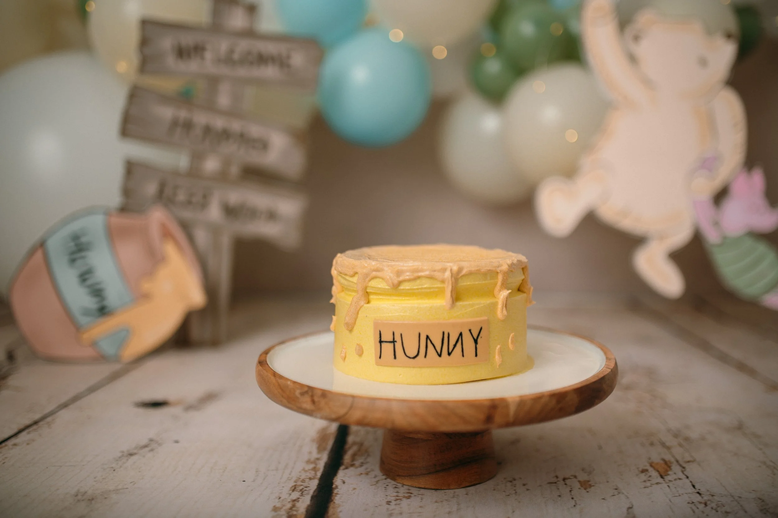 a cake that has the word hunny on it, the background is pooh bear themed, this is a setup for a cake smash first birthday baby celebration