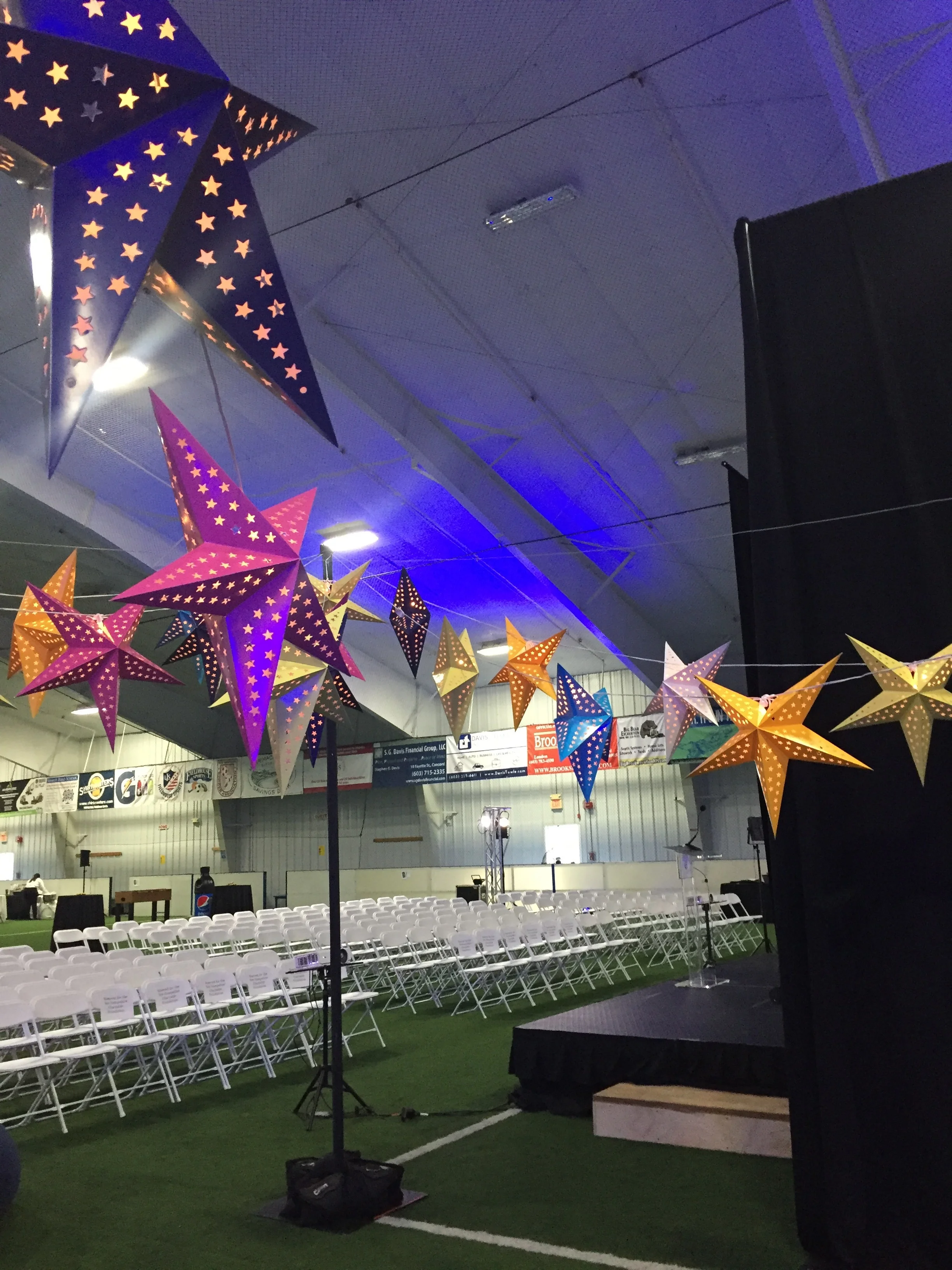 Star lanterns on cafe light strands installed with heavy bases and upright poles in a sports arena, Fieldhouse Sports , Bow, NH.