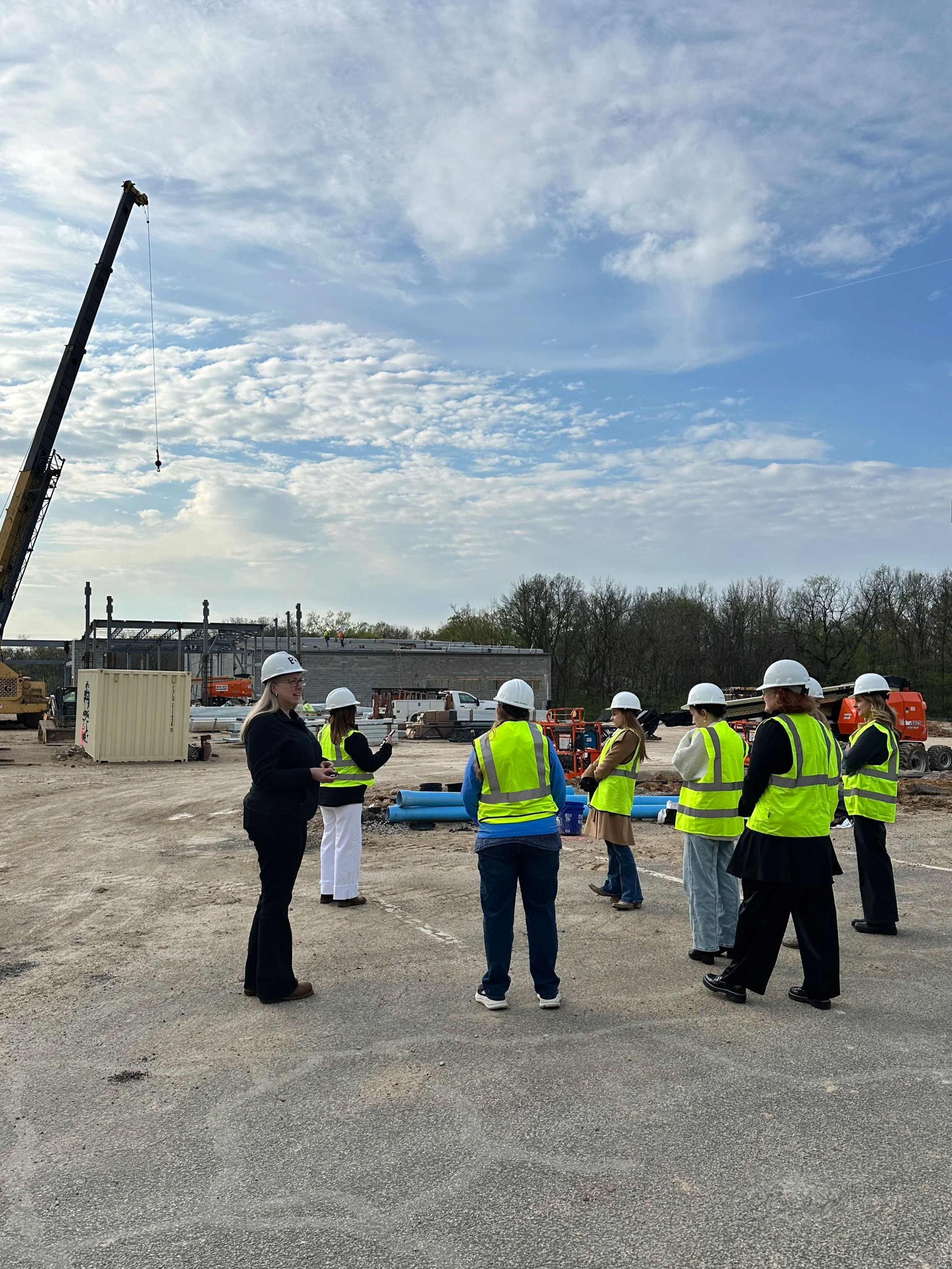 Group of construction workers and a supervisor wearing safety vests and helmets at a construction site.