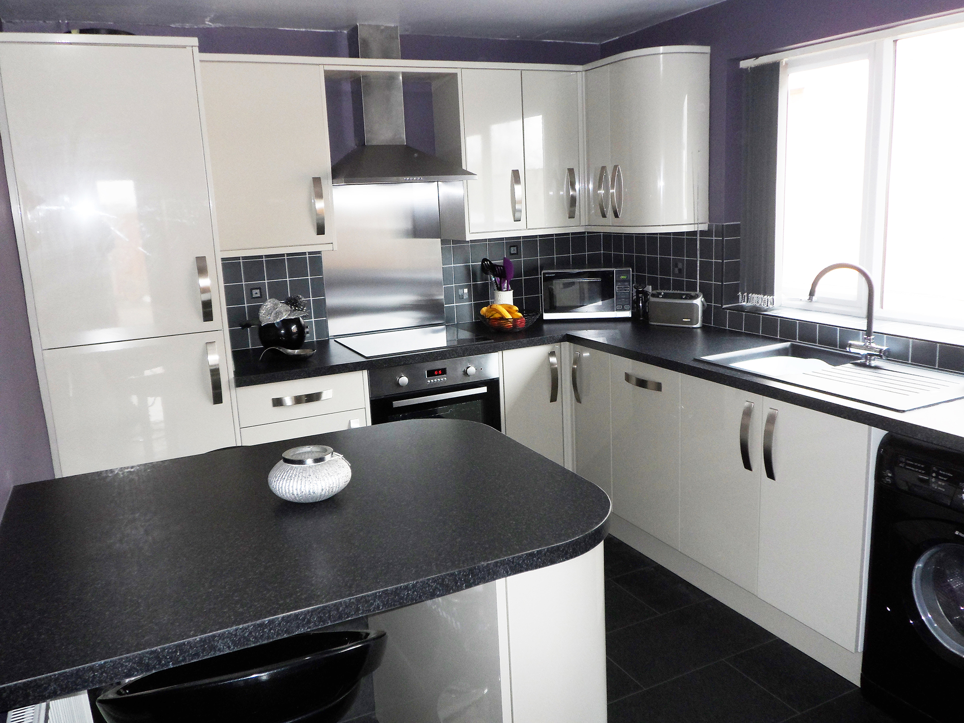 Gloss grey cabinets with black square edge worktops. Feature curved cabinets.