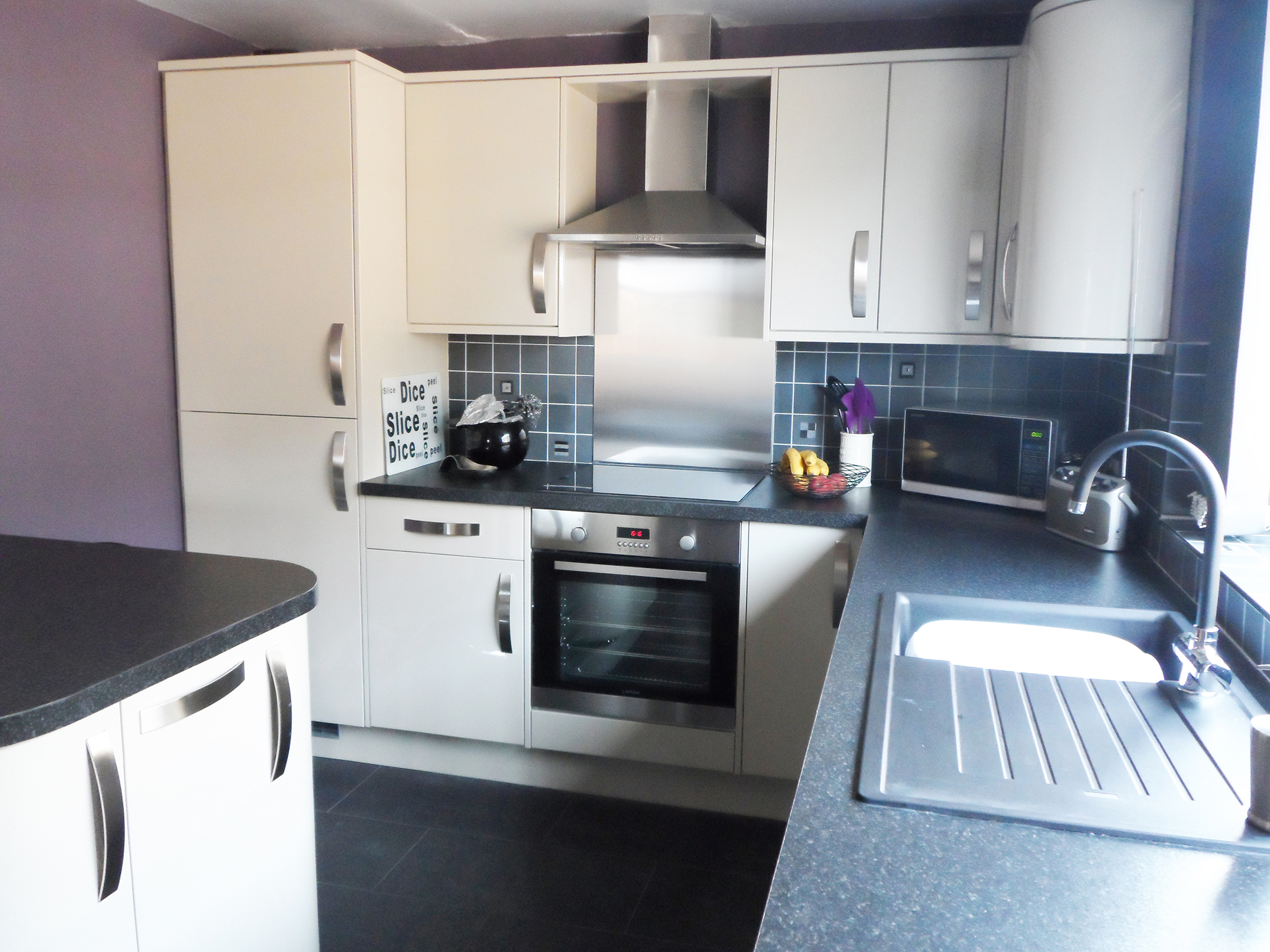 Gloss grey cabinets with black square edge worktops. Feature curved cabinets.