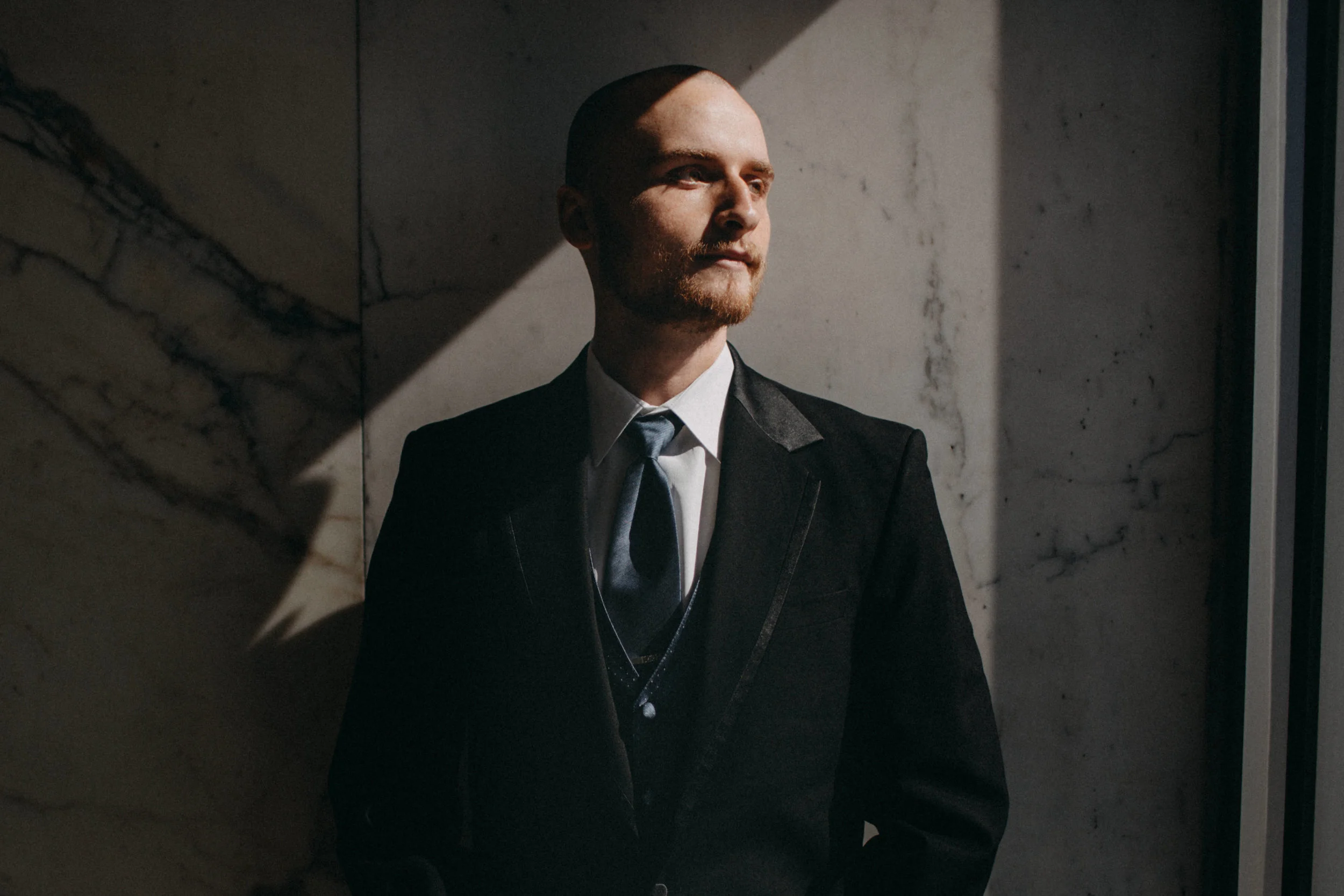Portrait of groom standing against wall.