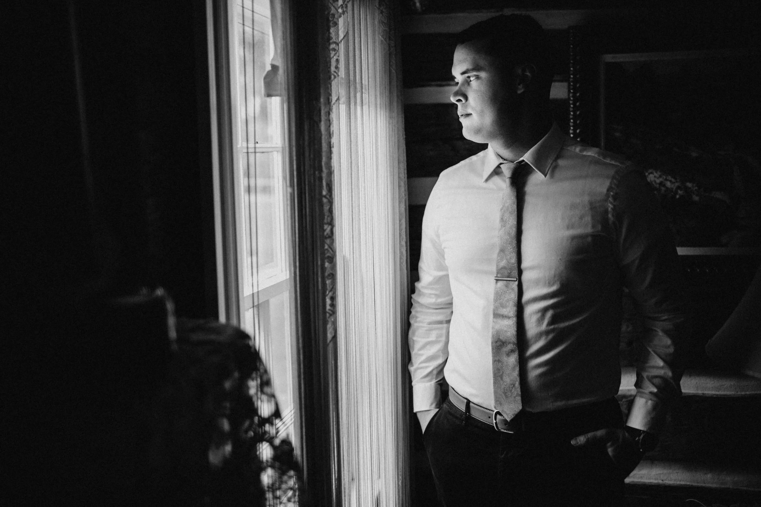 Portrait of groom standing beside window.