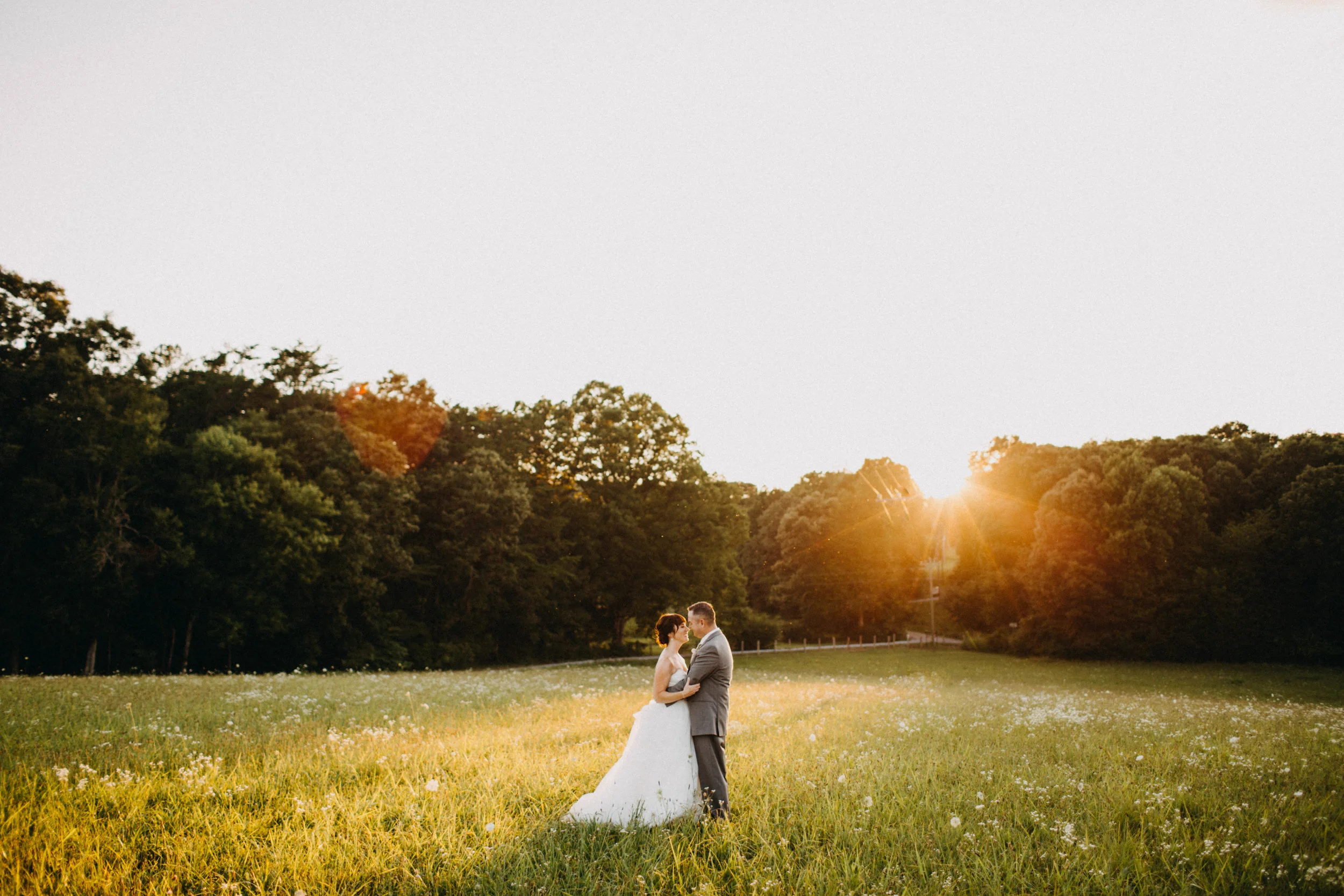 Portrait of couple standing in field at sunset.