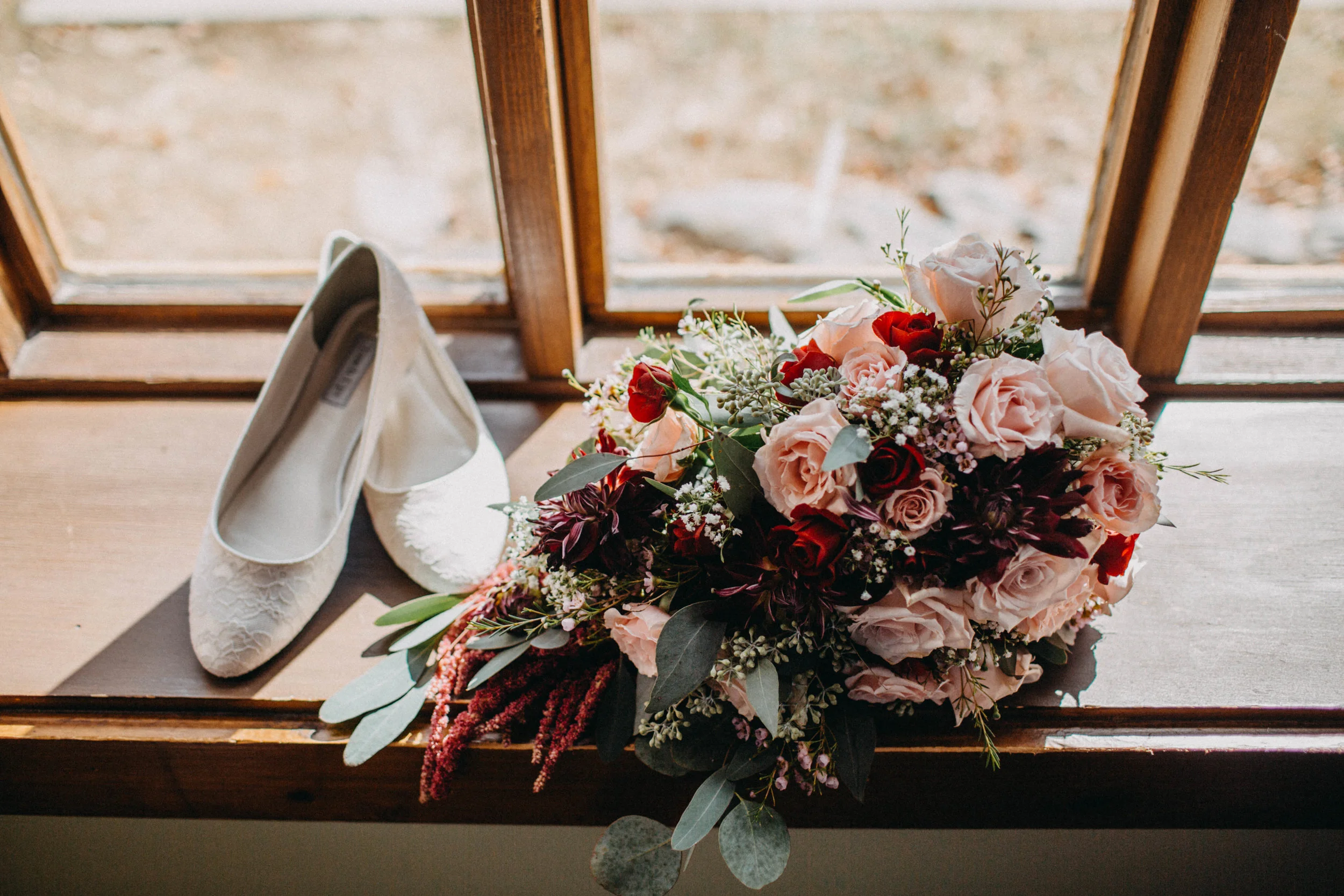 Photo of wedding shoes and bouquet on window sill.
