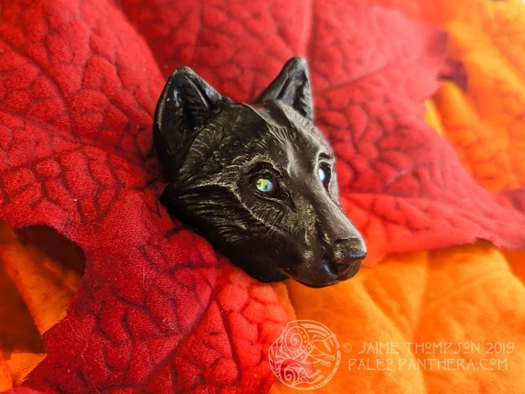 Oxidized black pewter wolf with orange metallic glass eyes.