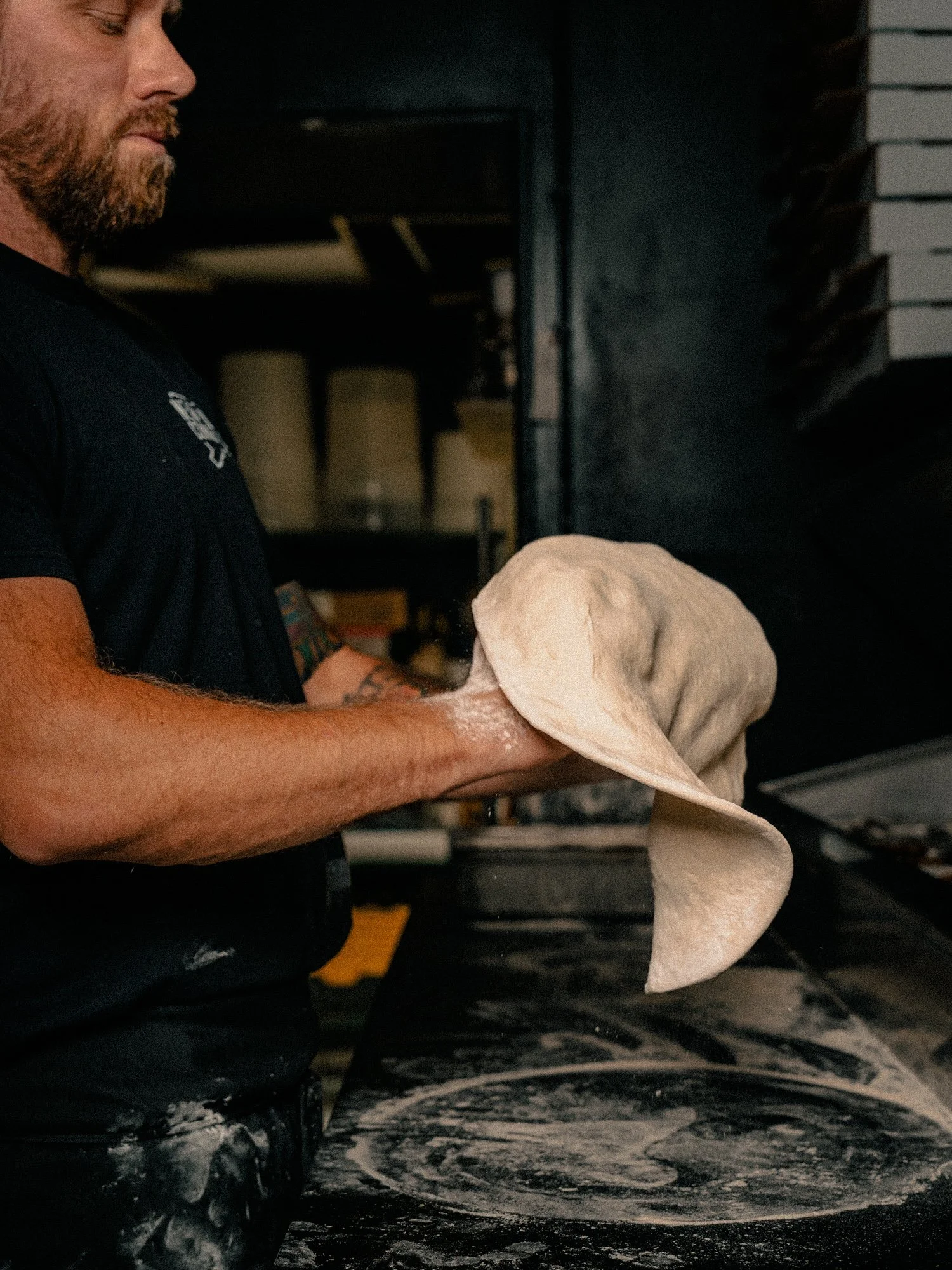 Andrew stretching pizza dough by hand at the counter in One6Three's kitchen