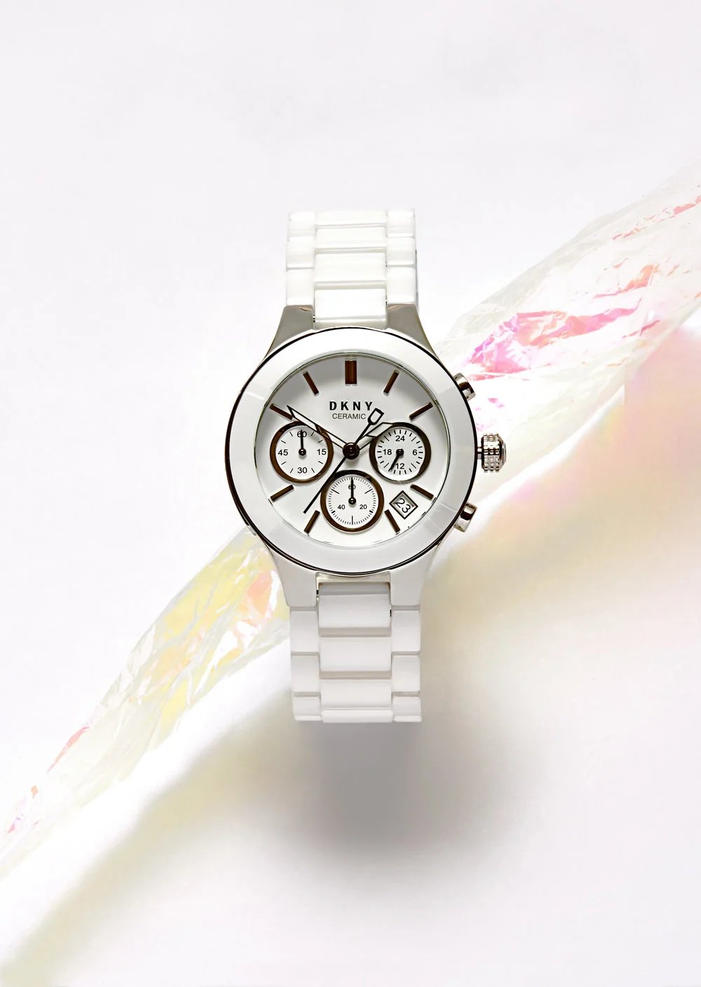  A white DKNY watch floating in white background with multi coloured water splash running through centre of DKNY watch. Still Life Photograph by London Based Still Life Photographer Andy Carson 