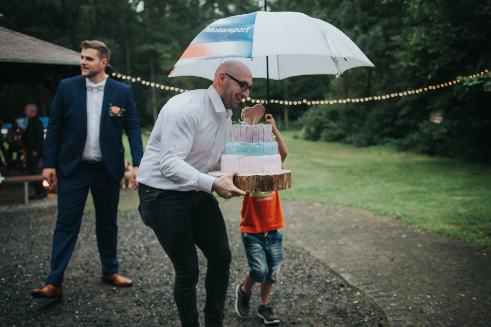 Hochzeitsgast trägt Torte unter Regenschirm