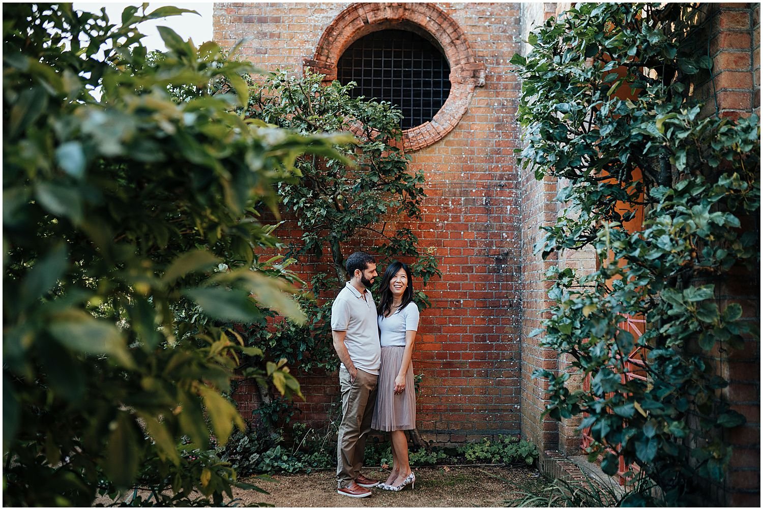 Couple standing by old brick wall in Pergola and Hill Gardens