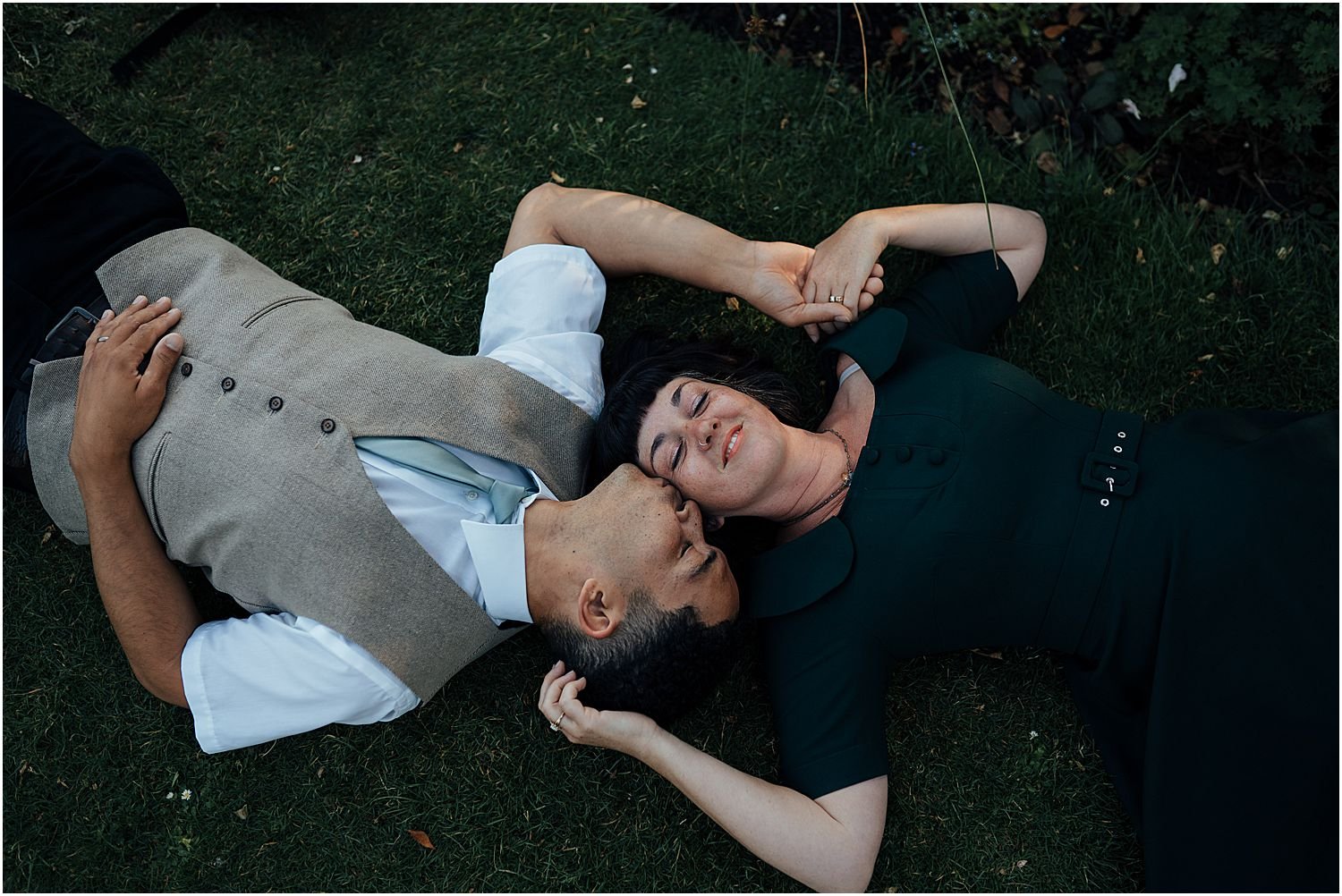 Engaged couple lying down in grass in park in summer